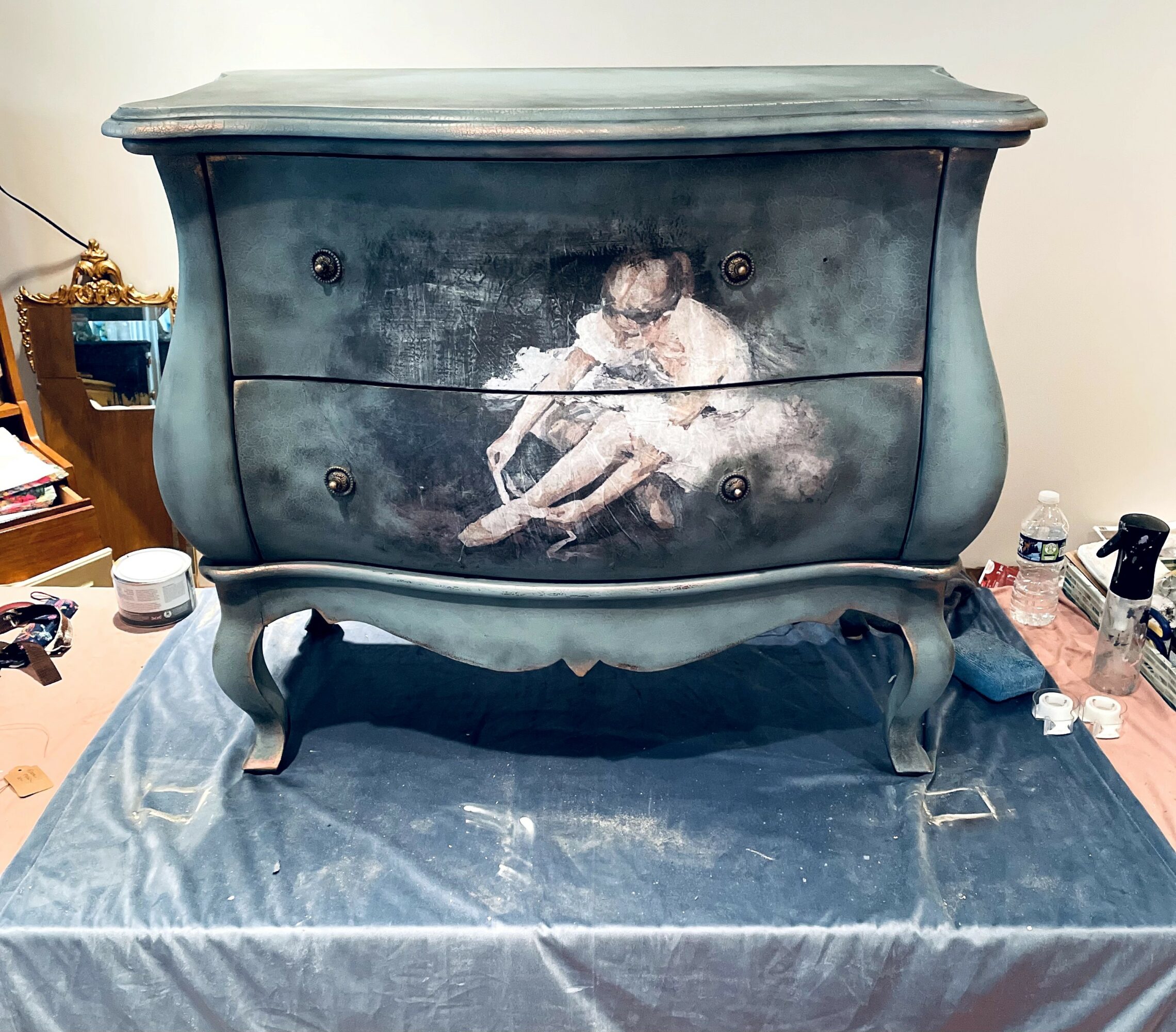 Dark-colored dresser with a painting of a child sitting on the ground, holding a stick, painted on the front.