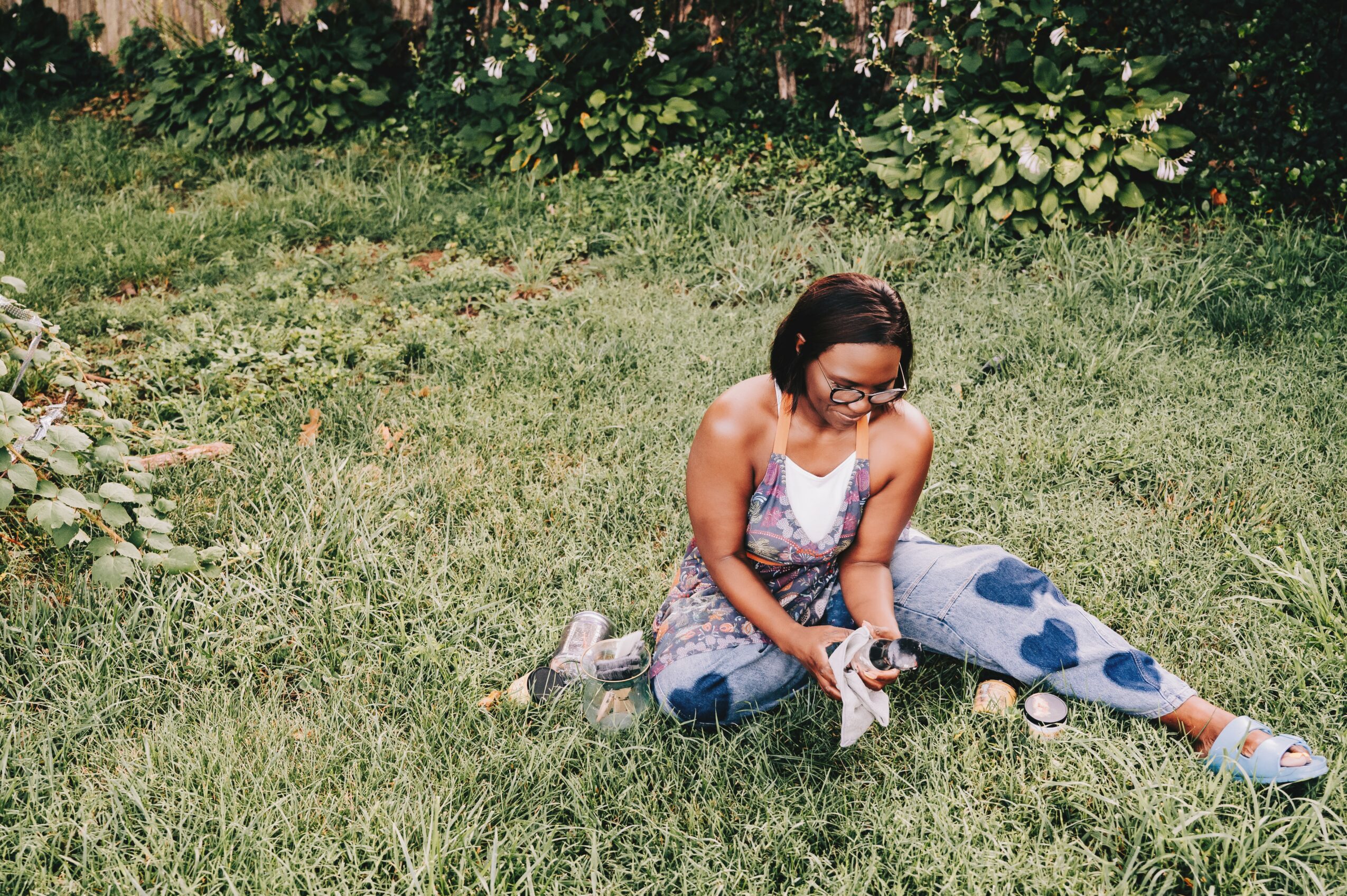 Girl sitting on grass with plants in background, wearing glasses and a patterned dress.