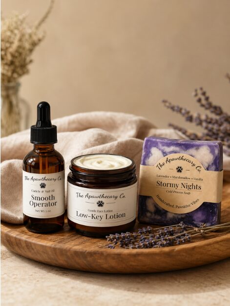 Brown glass dropper bottle, jar of lotion, and a purple and white soap on a wooden tray with lavender sprigs.