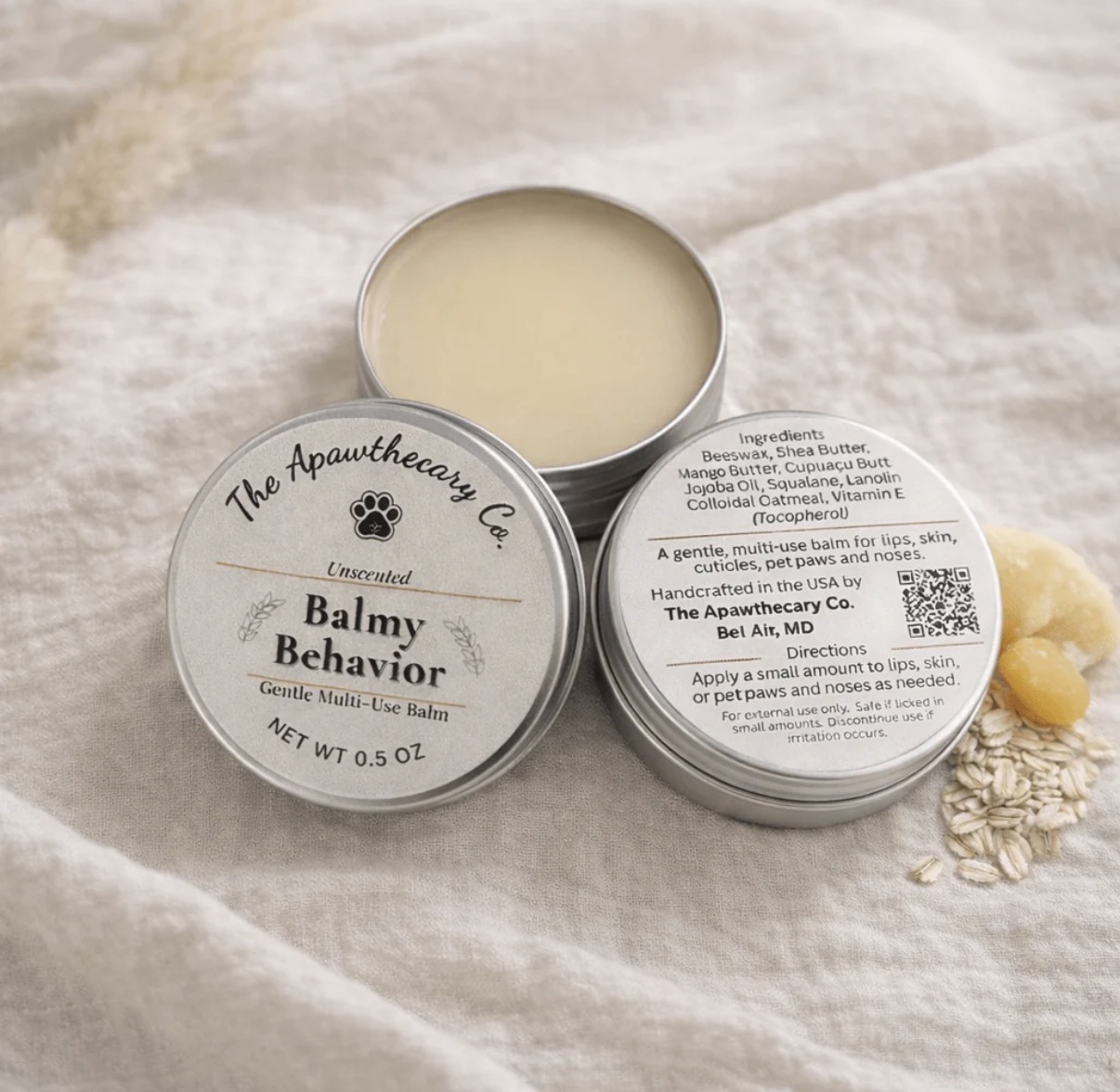 Open tin of Balmy Behavior beard and moustache balm on fabric with oats and a cloth in background.