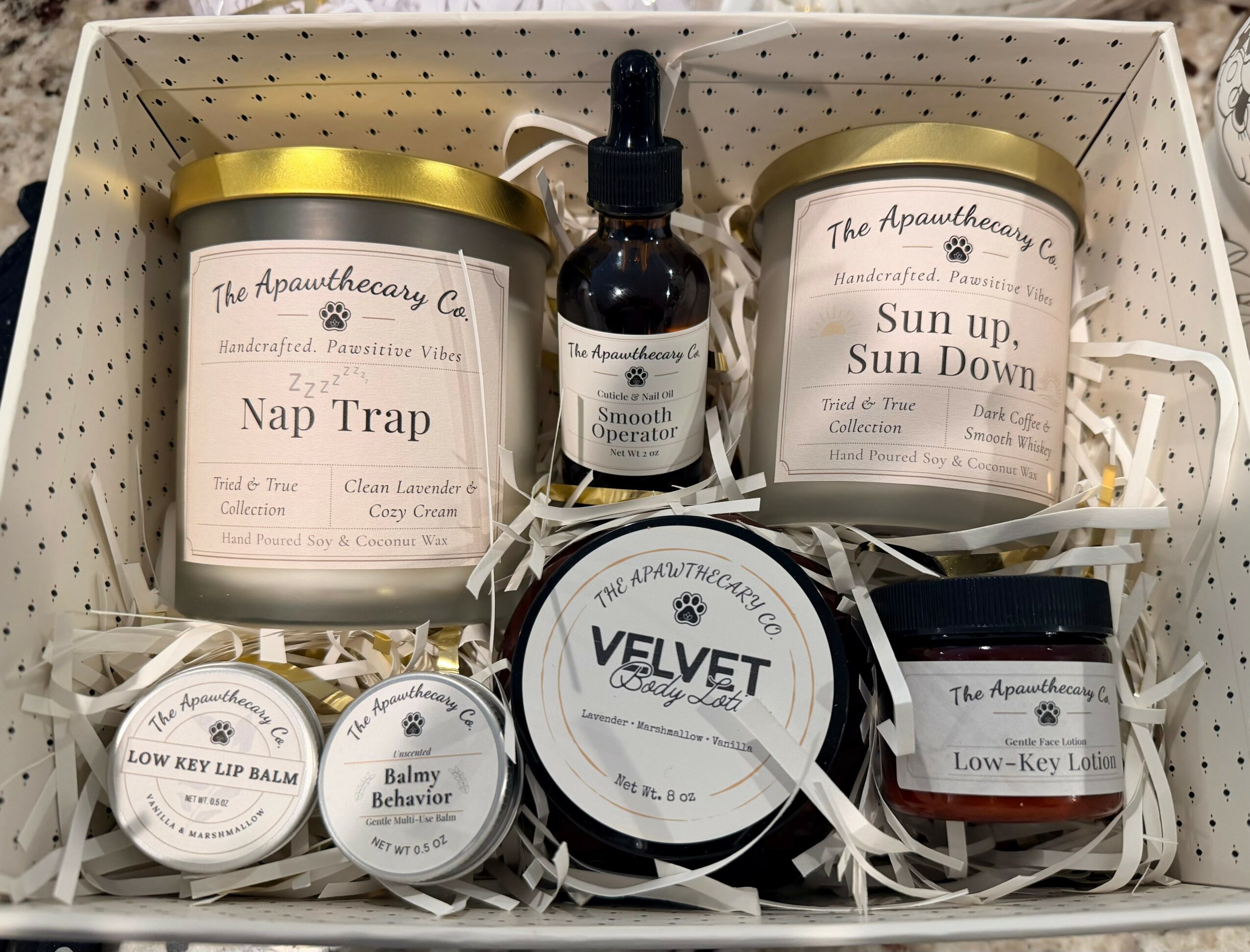 Gift box with candles, balm, and spray bottles, all labeled with natural or herbal product names, arranged neatly.