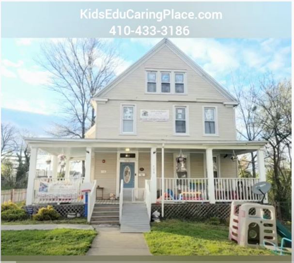 Three-story house with a front porch, white railing, and steps leading to the entrance, surrounded by grass and trees.