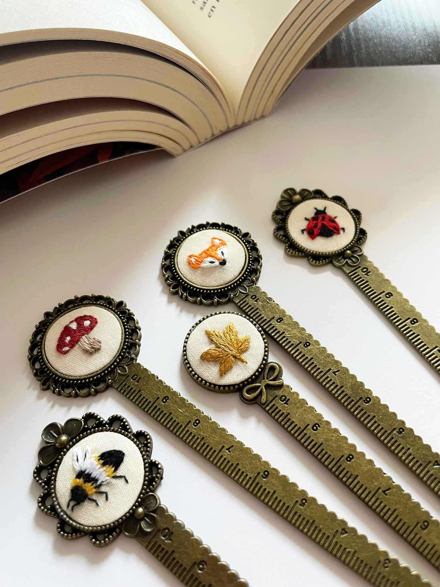 Four decorative bookmarks with animal and insect images, placed on a white surface near an open book.