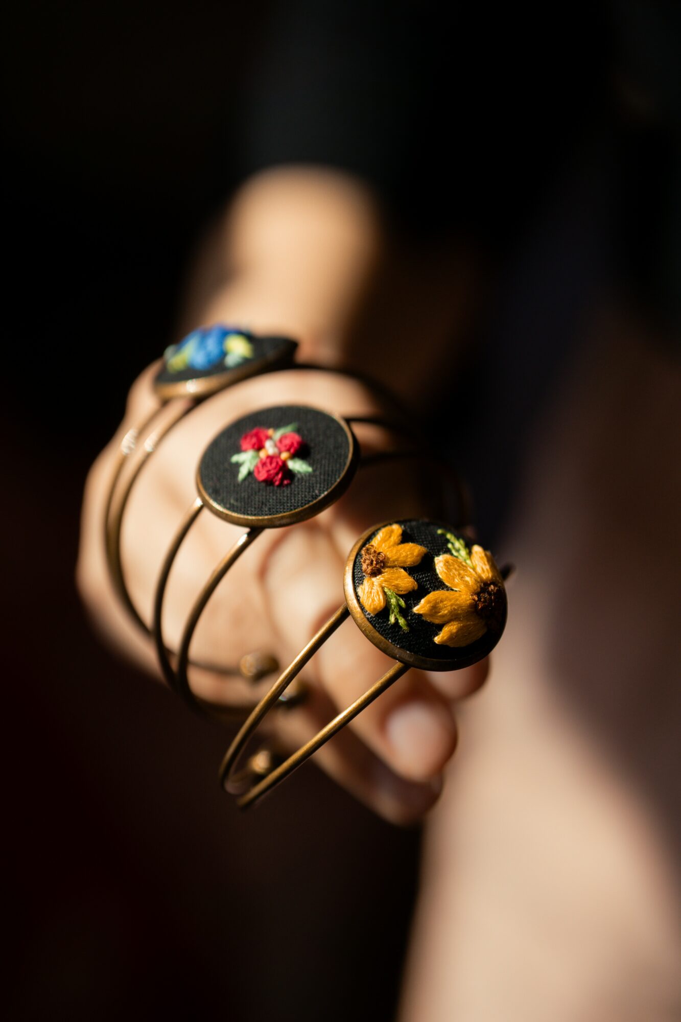 Person holds three hairpins with embroidered floral designs on black circular bases.