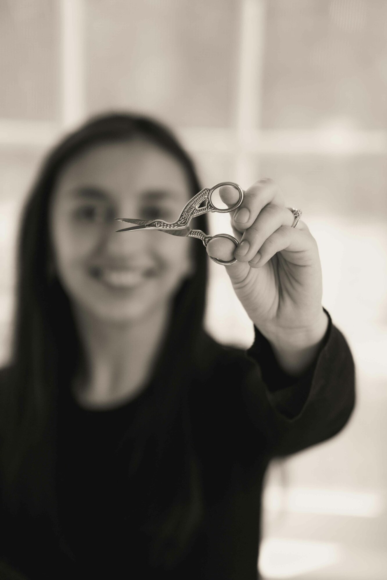 Person holding small scissors towards the camera, smiling, with a blurred background.