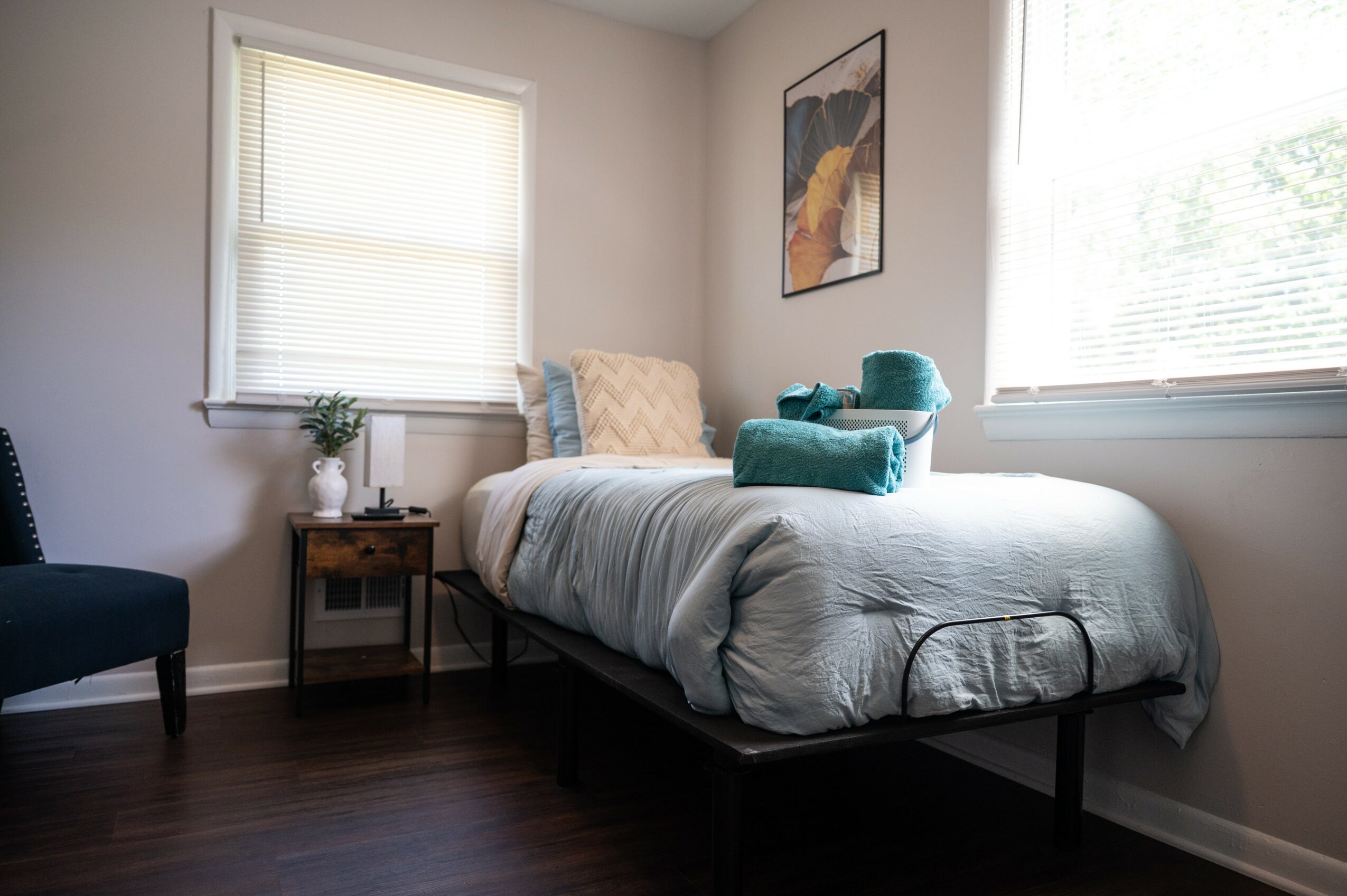 Bedroom with bed, window, small side table, and artwork on wall.