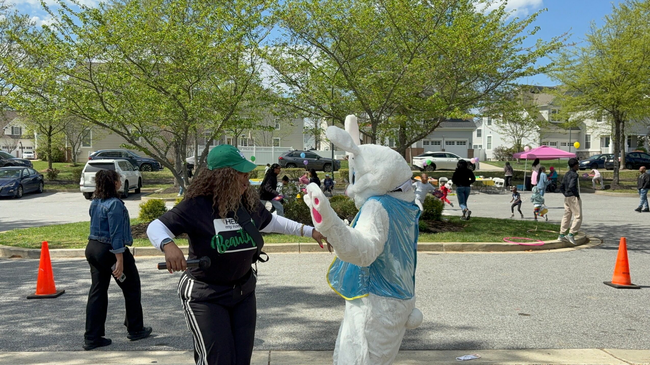 Person in a bunny costume talking to a woman outdoors with trees and people in background.