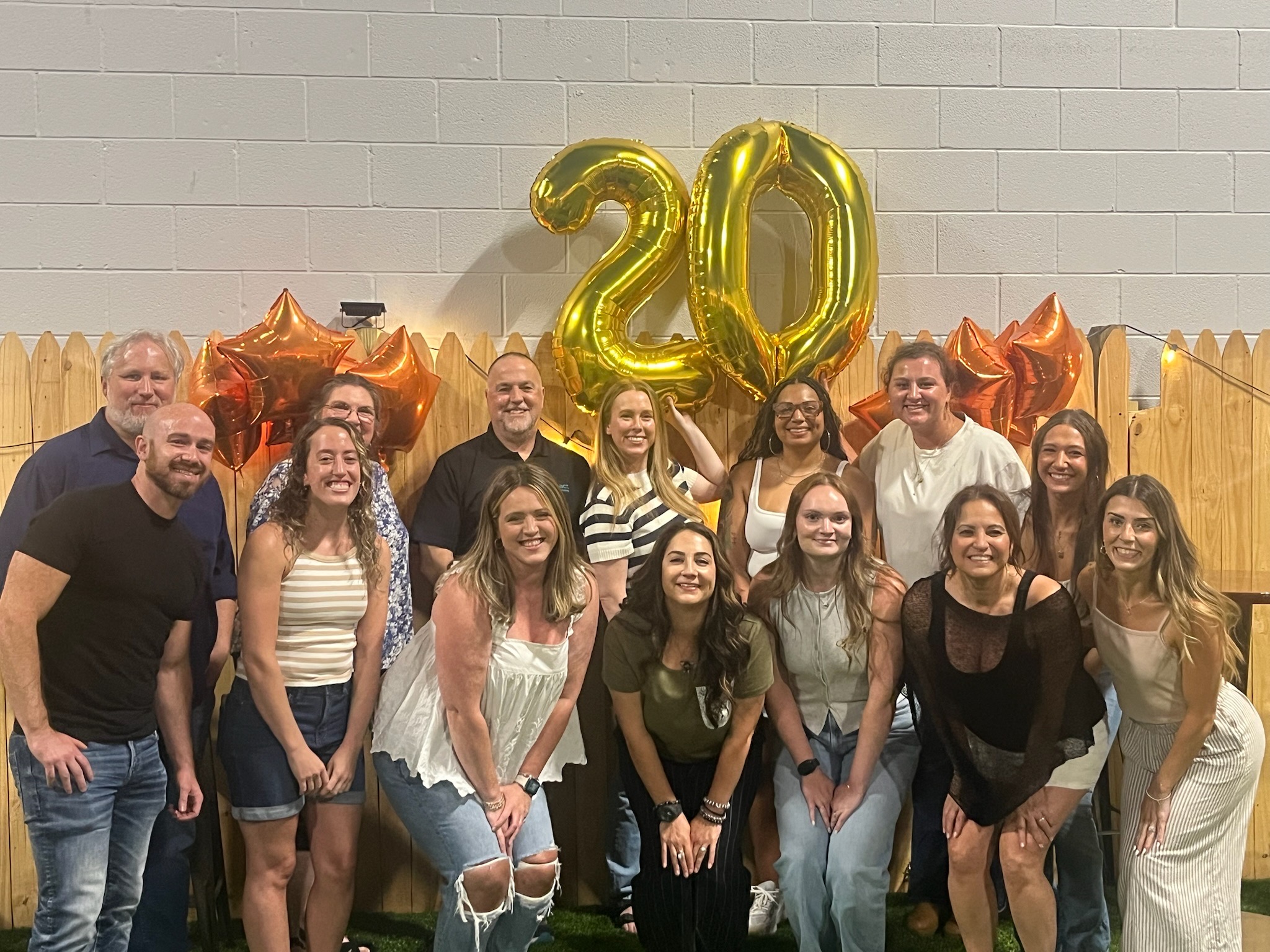 Group of people celebrating 20th anniversary with balloons and decorations, smiling for the photo.
