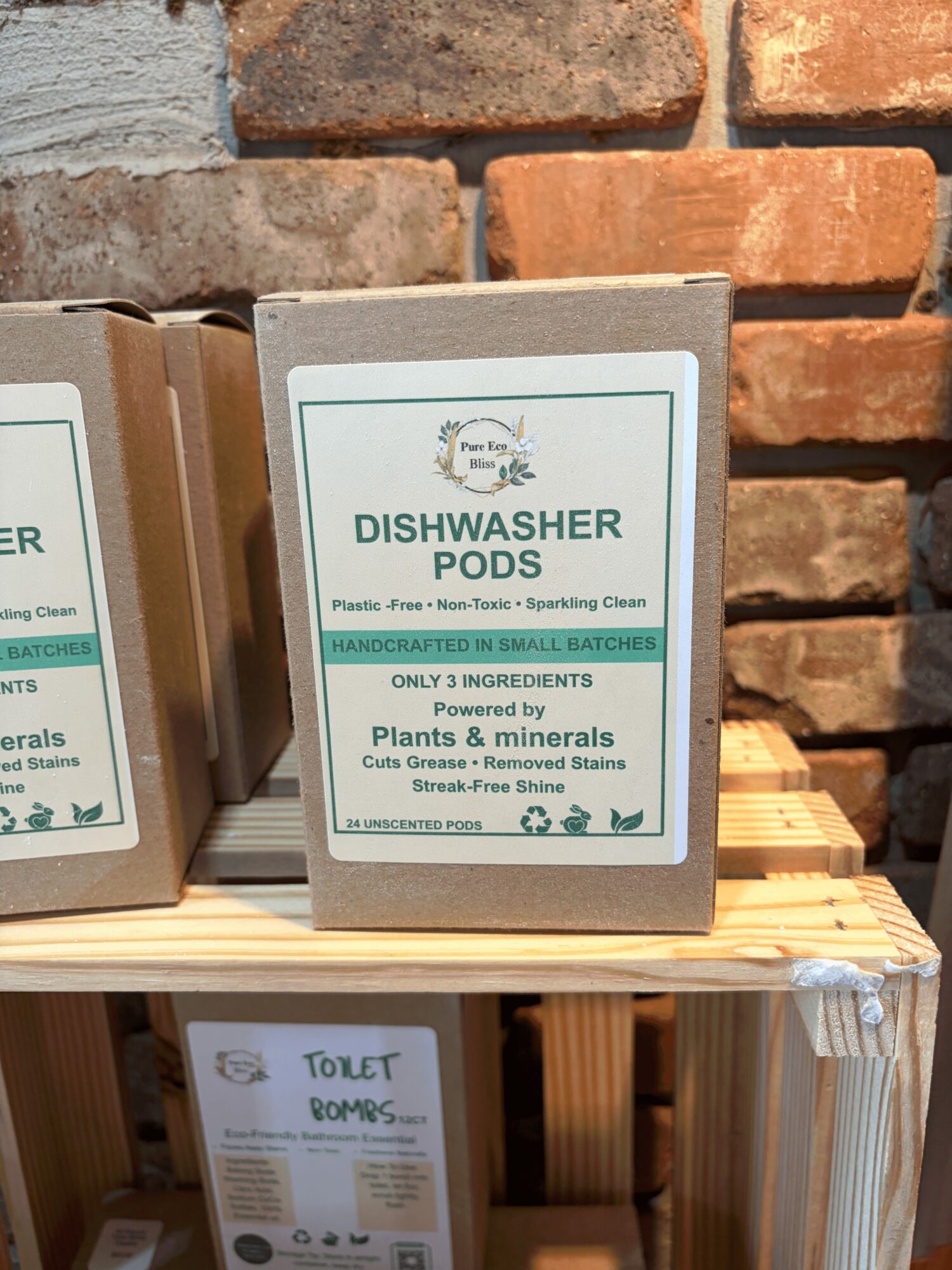 Box of dishwasher pods on a wooden shelf against a brick wall background.