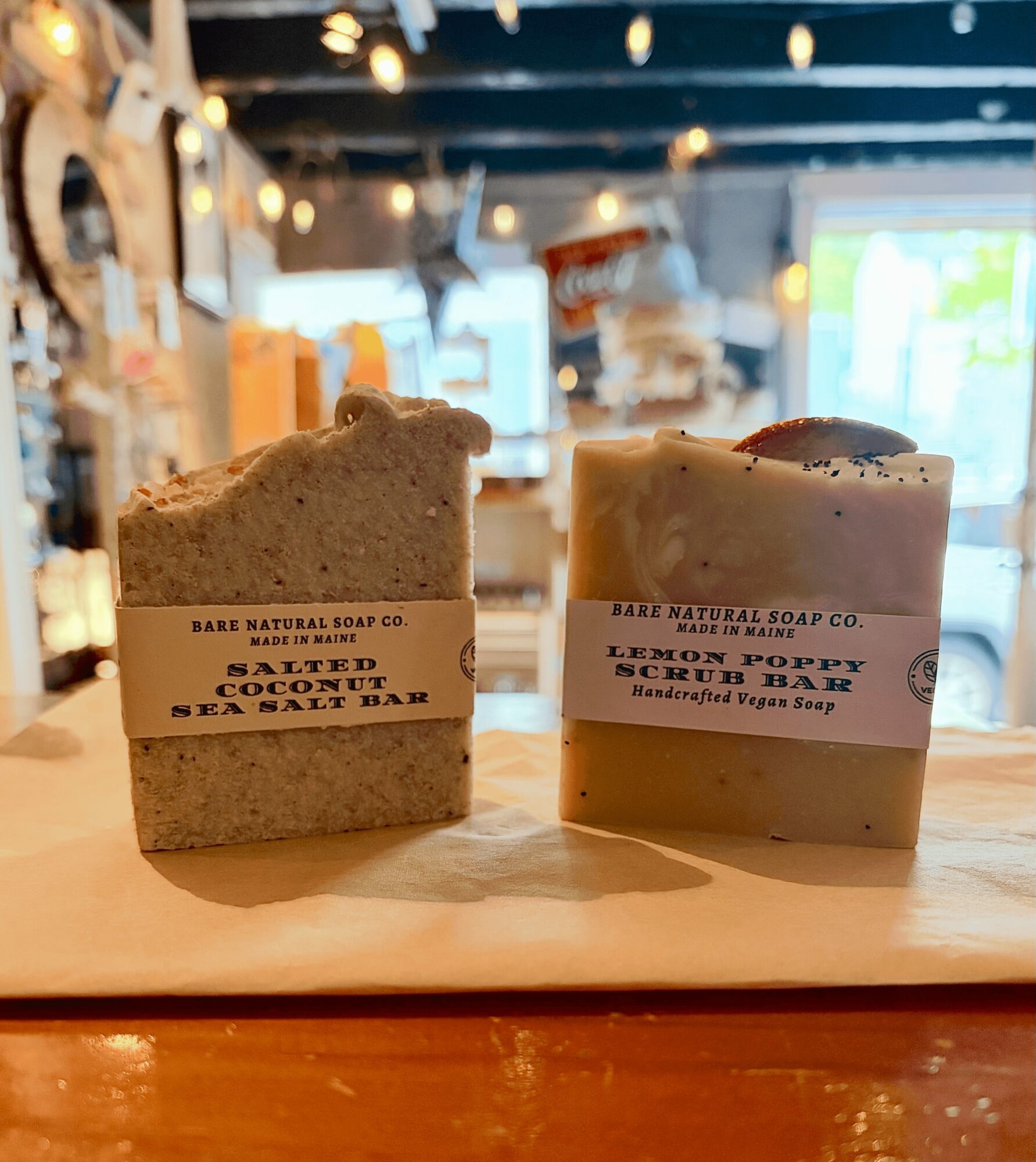 Two handmade soap bars on a wooden surface with blurred store interior in background.