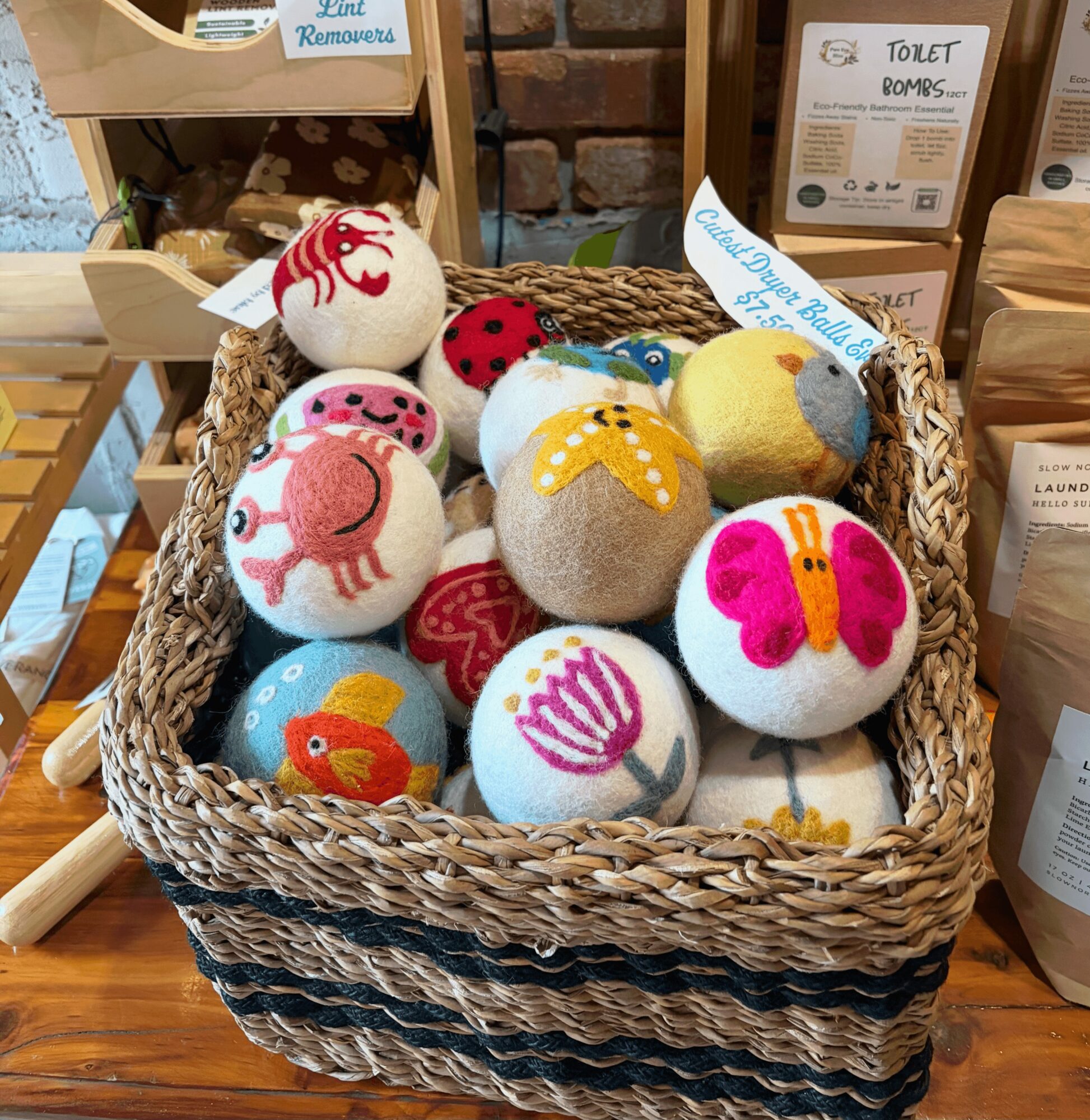 Basket filled with colorful felted balls with various patterns and designs, placed on a wooden surface.