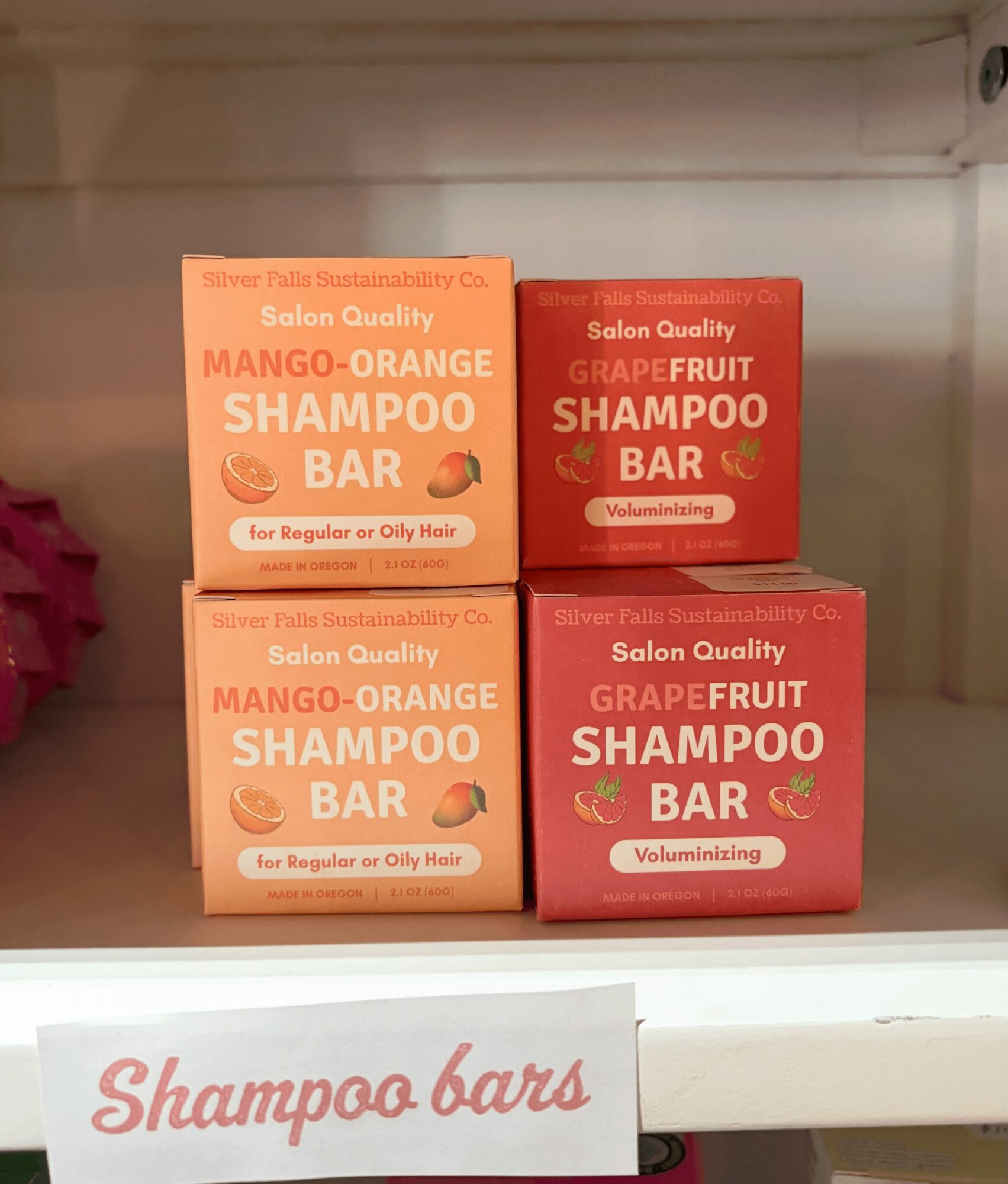 Four boxes of shampoo bars on a shelf, two orange and two red, with a white sign reading 'Shampoo bars'.