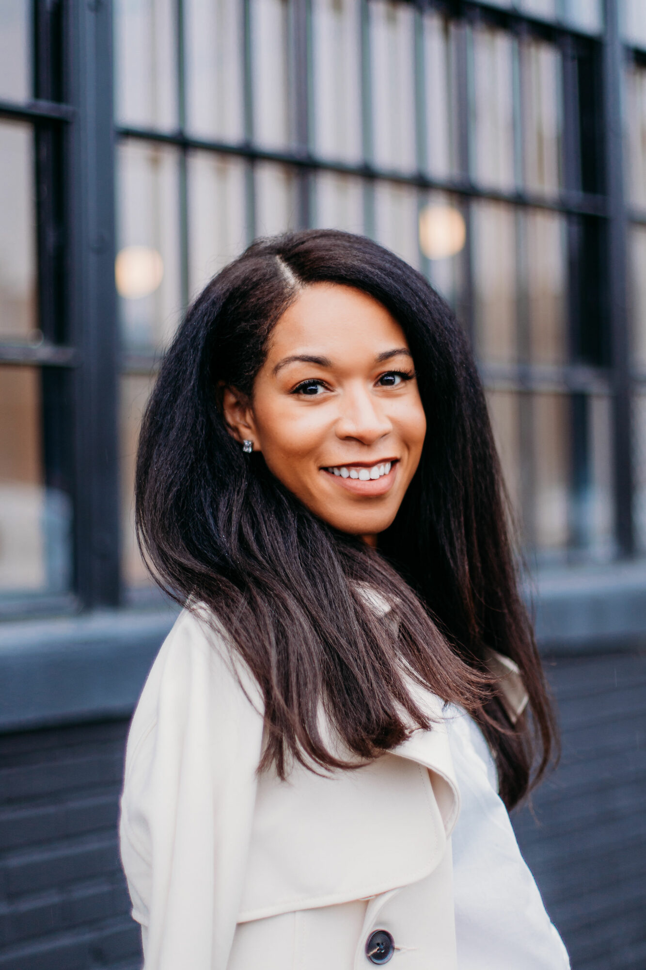 Smiling woman with long dark hair standing outdoors in front of a metal fence.