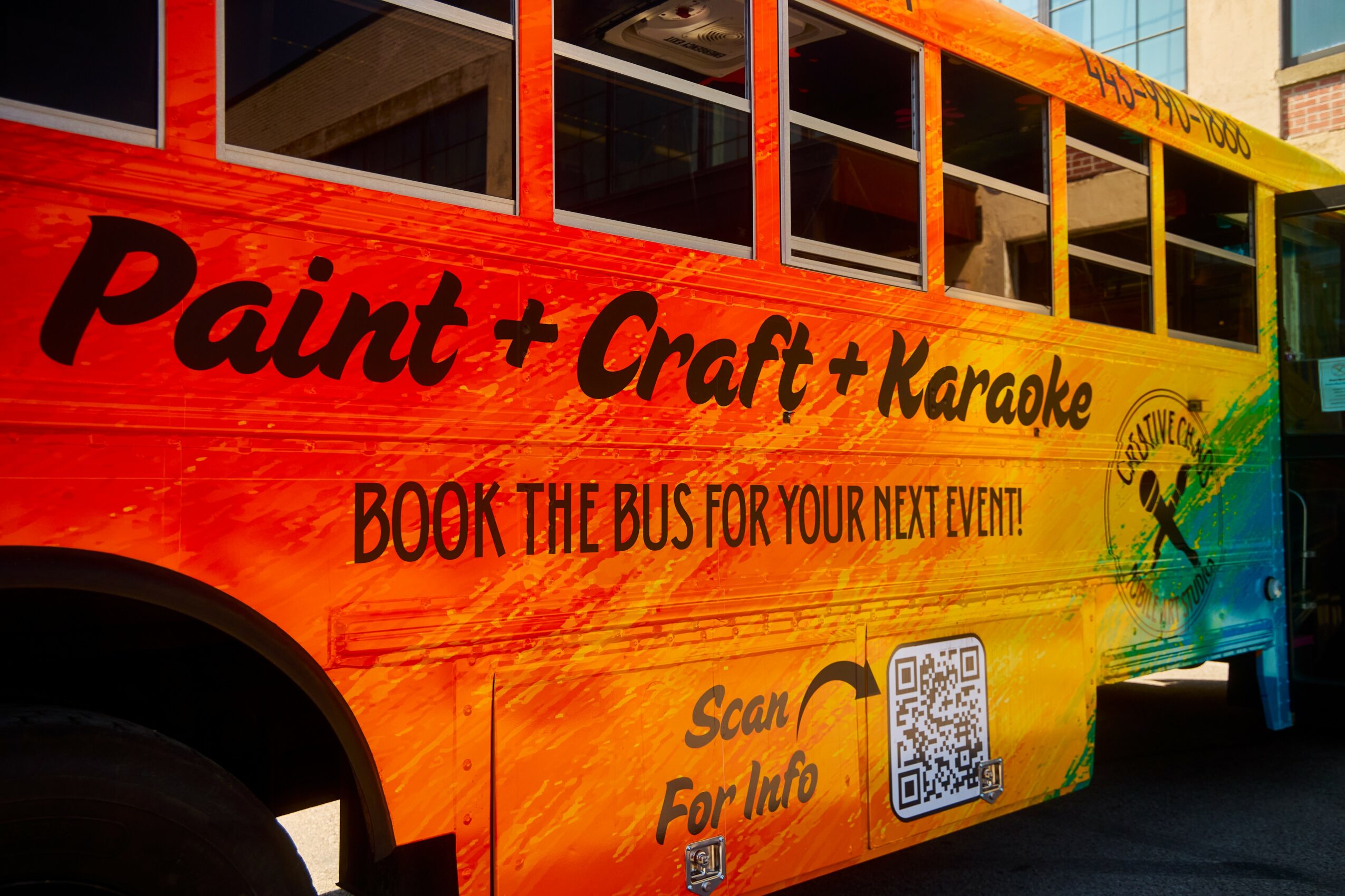 Colorful bus with text advertising paint, craft, karaoke, and a QR code for information.