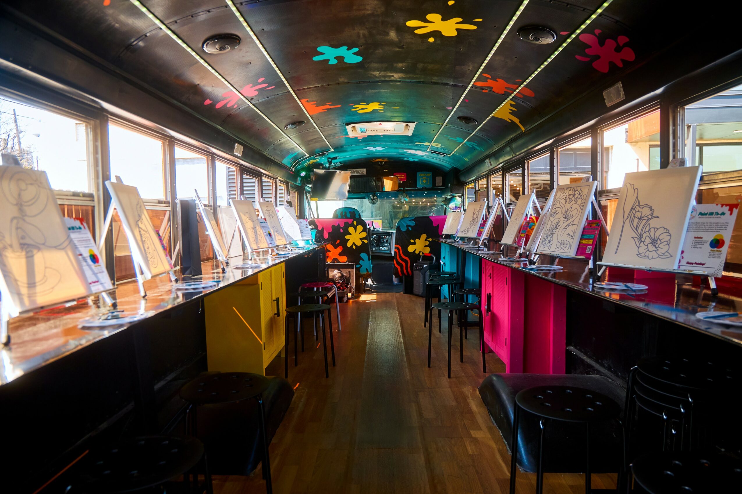 Interior of a brightly decorated art gallery with colorful flower patterns on the ceiling and display tables along windows.