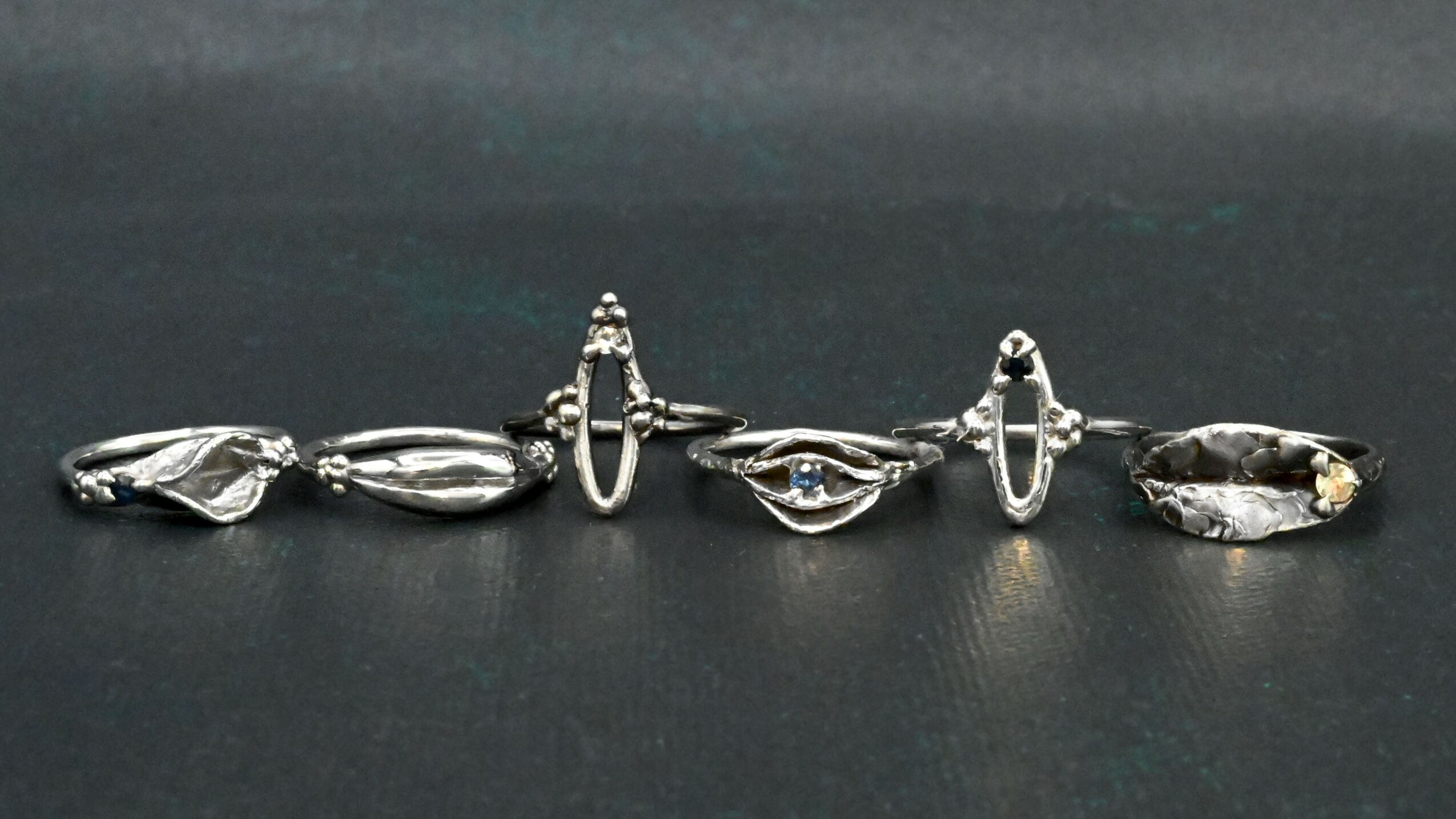 A row of five metallic objects with elongated shapes and textured surfaces, arranged on a dark background.