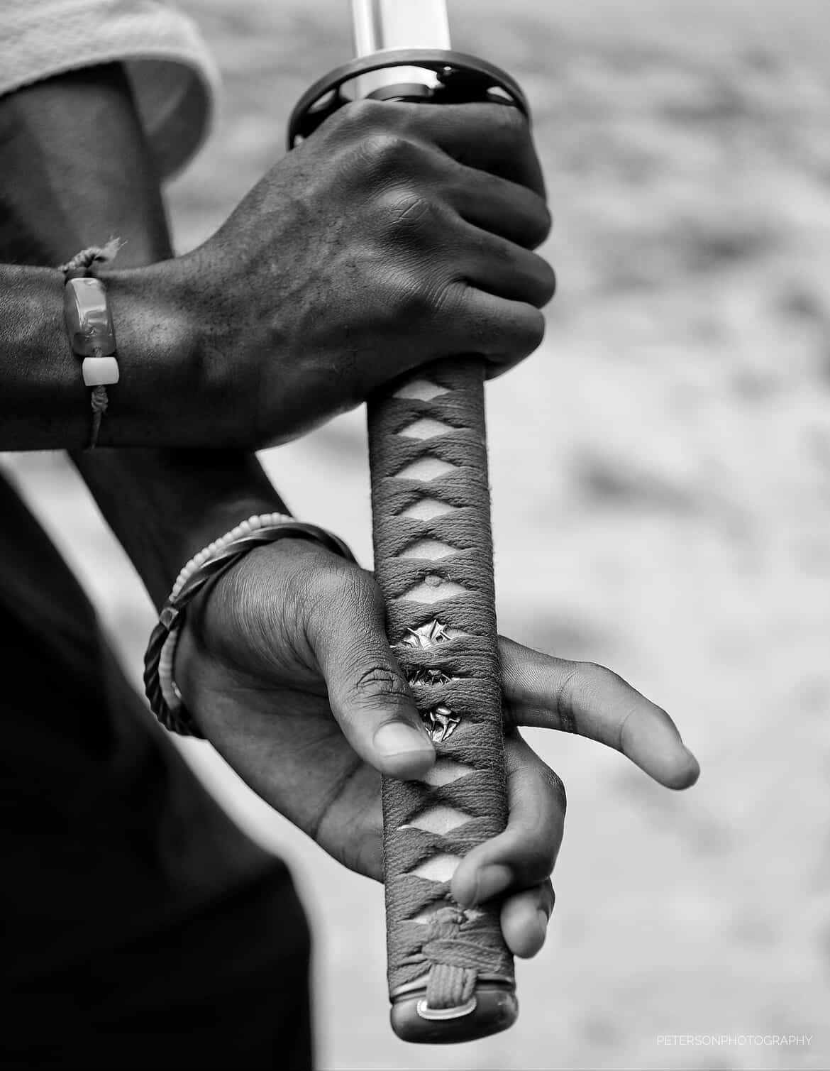 Two hands gripping a sword handle, one hand above the other, with a blurred background.