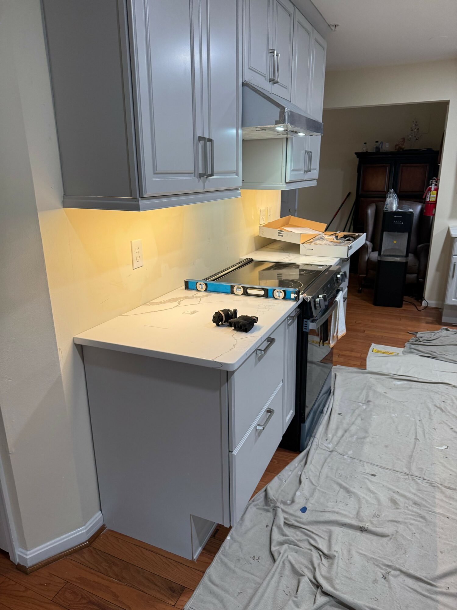 Kitchen with gray cabinets, countertop, and a level tool on the counter. Partially covered floor with a cloth.