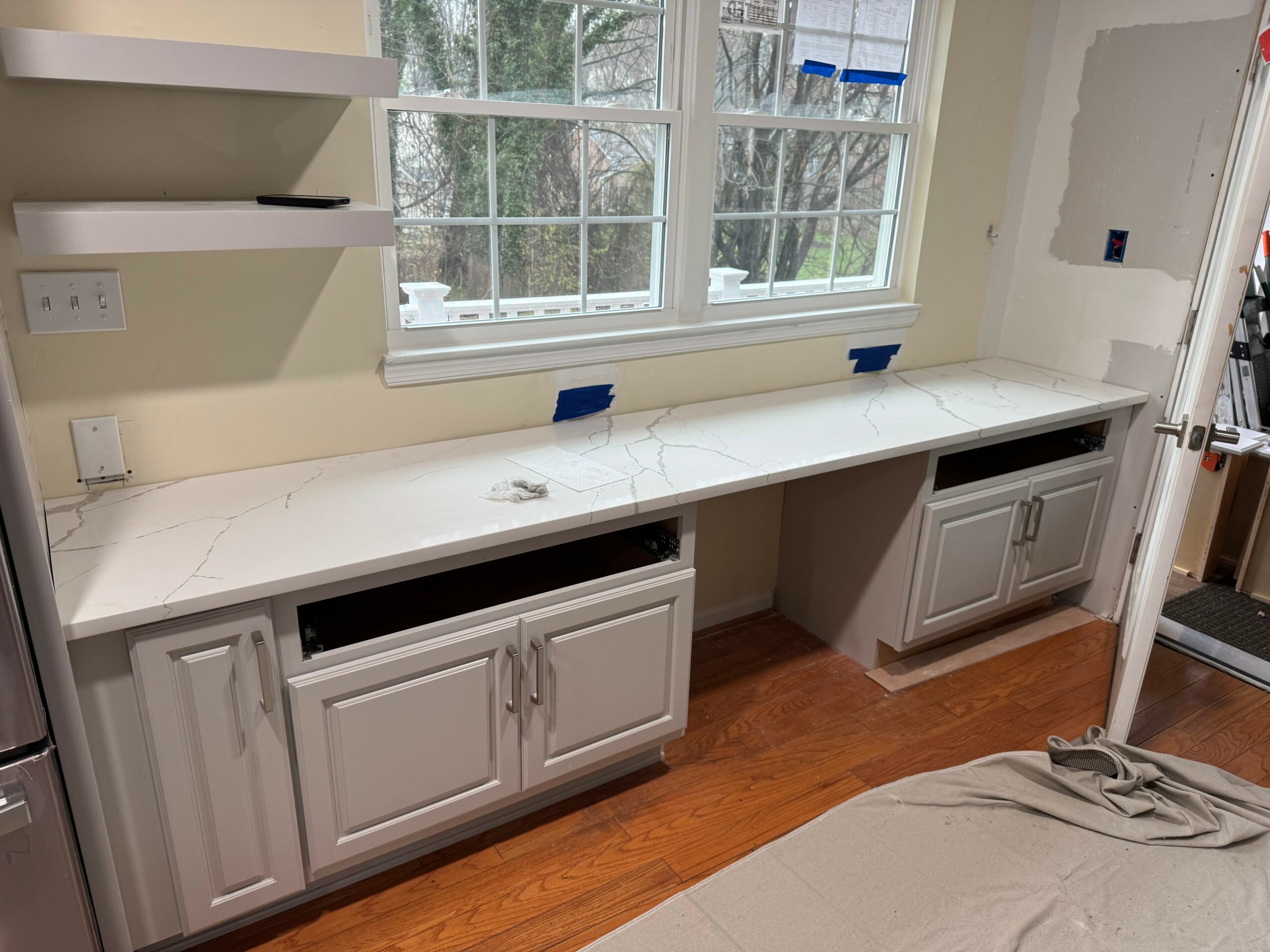 Long white countertop with cabinets below, window above, and a wall with an opening on the right side.