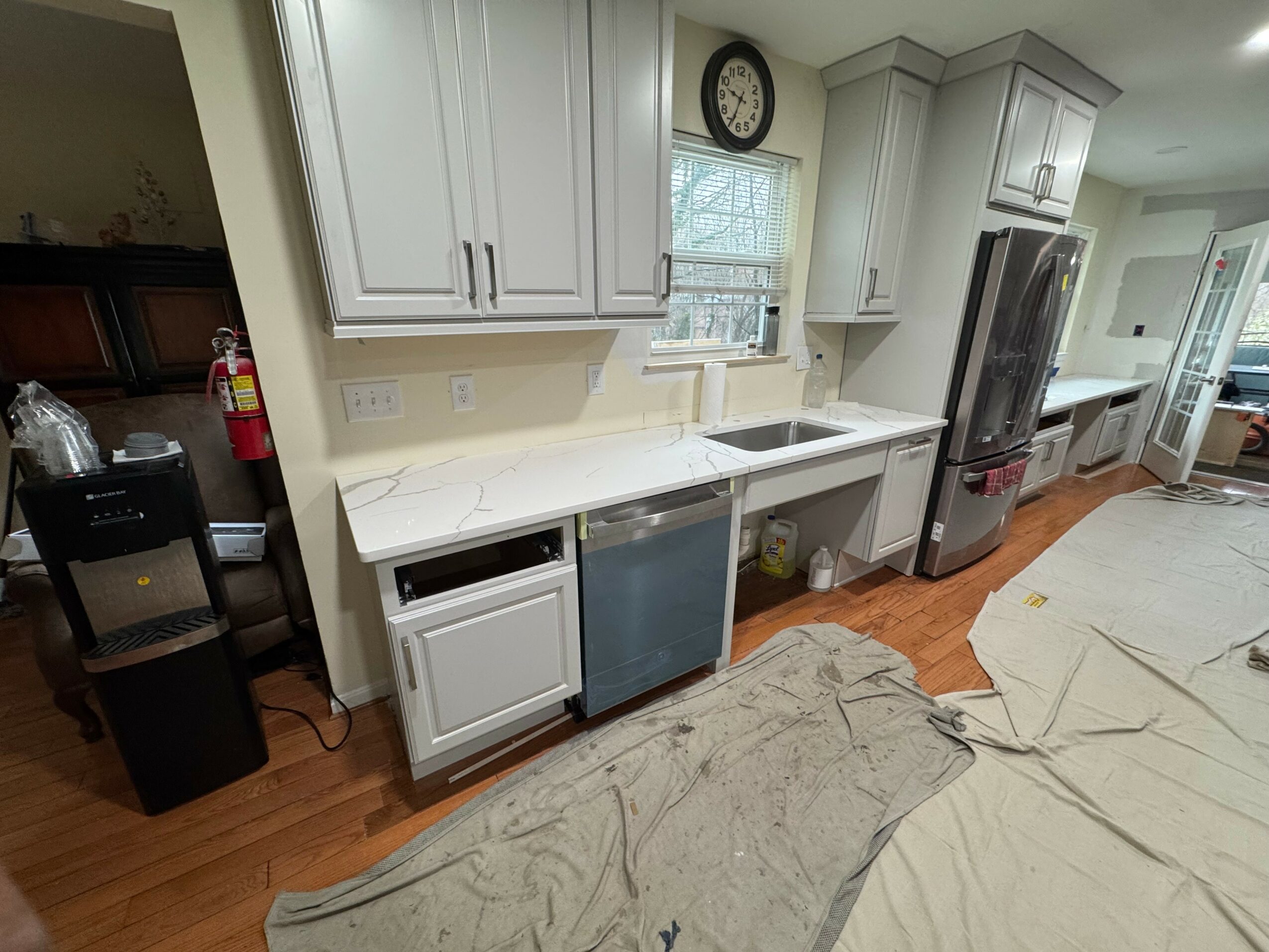 Kitchen with white cabinets, a window above the sink, a clock, and a dishwasher. A countertop extends along the wall.