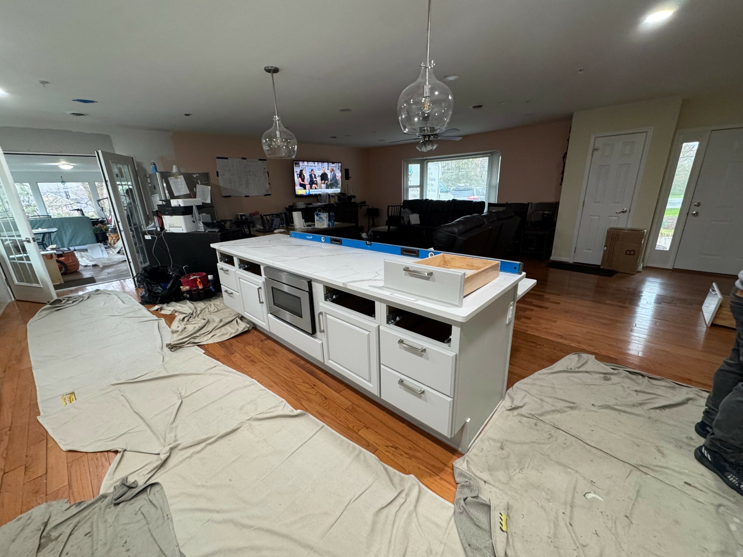 Kitchen island with white cabinets and a white countertop in a spacious open living area, with hardwood floors and hanging pendant lights.