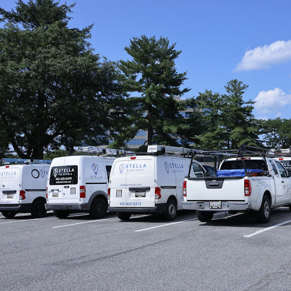 Row of white vans and trucks parked in a parking lot with trees and blue sky in background.