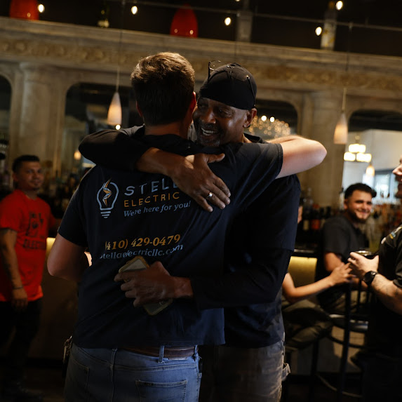 Two men hugging in a lively indoor setting with other people in the background.