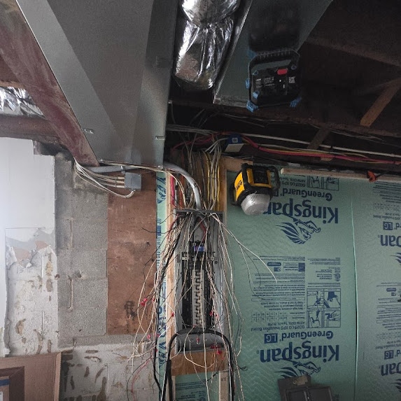 Electrical wires and cables hanging near a wall with insulation material and a metal box.