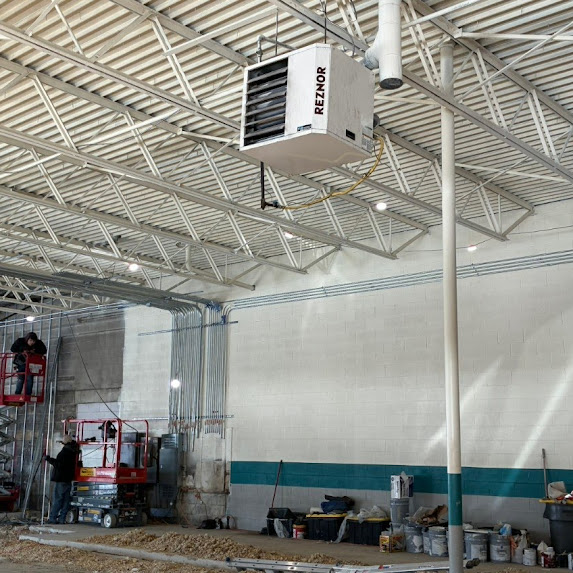 Industrial space with ceiling-mounted air conditioning unit, workers, and equipment along a wall.