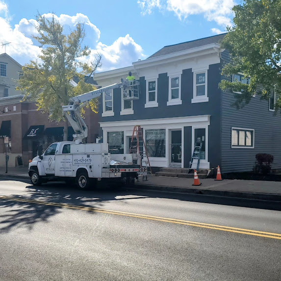 Workers in a bucket lift painting the upper part of a two-story building with dark siding and white trim.