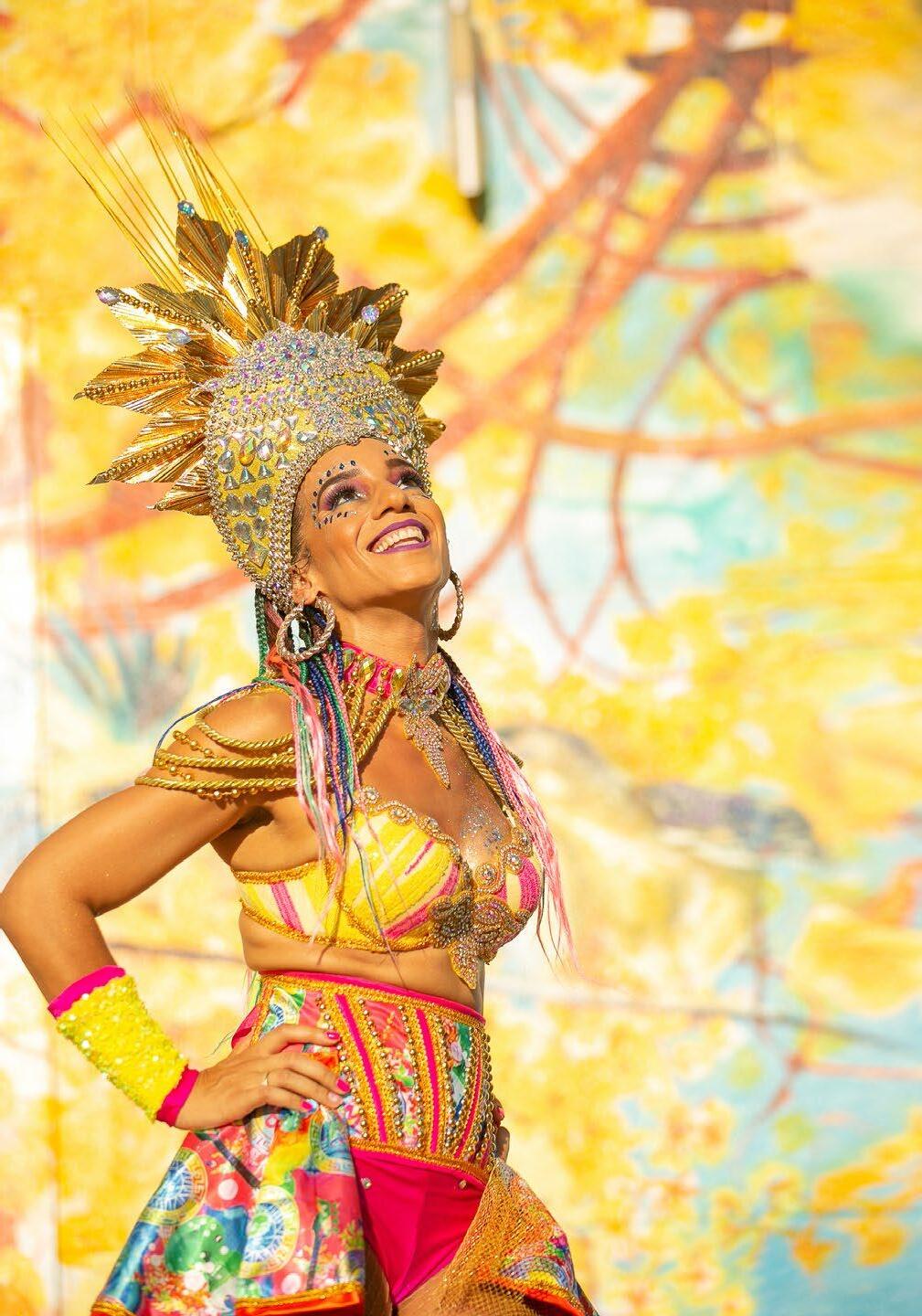 Woman in colorful costume with elaborate headdress smiling against a vibrant background.