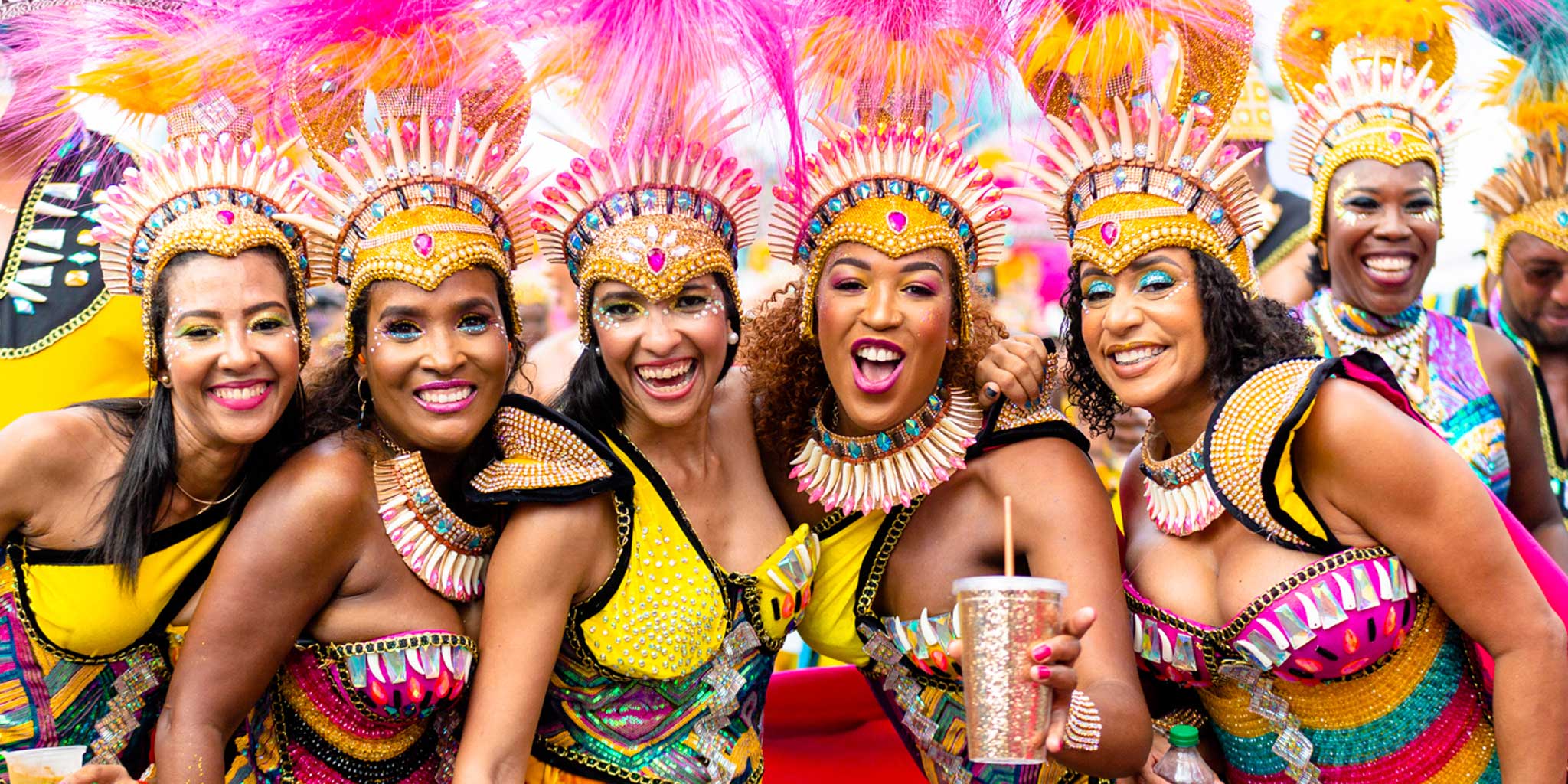 Group of women in colorful traditional costumes and headdresses smiling together.