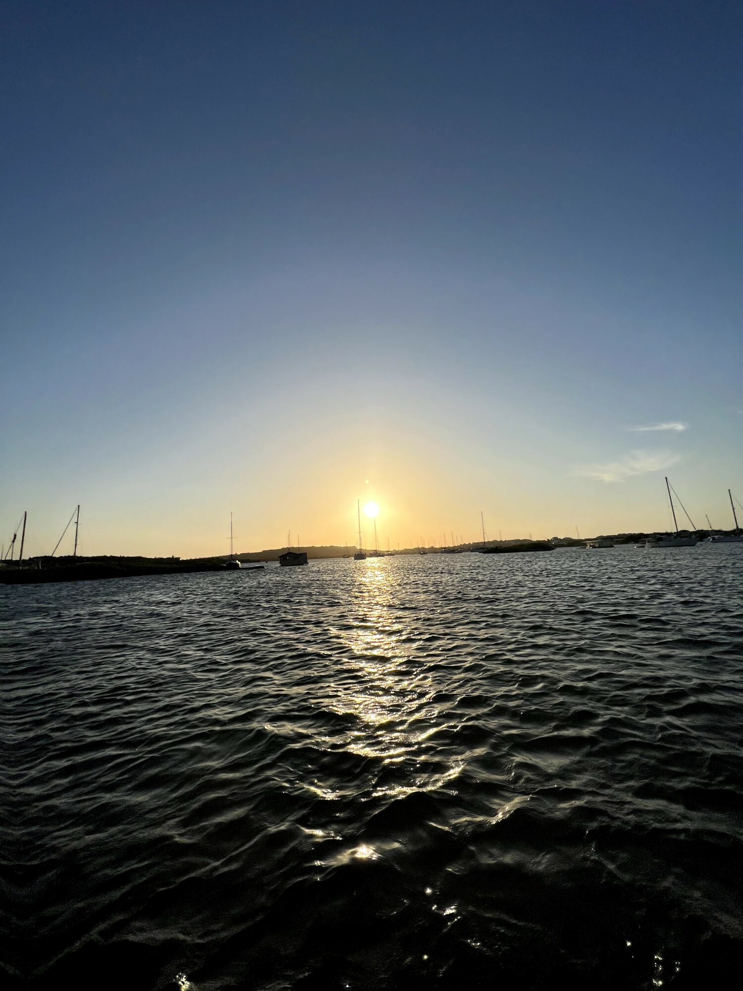 Sunset over a body of water with boats and a clear sky.