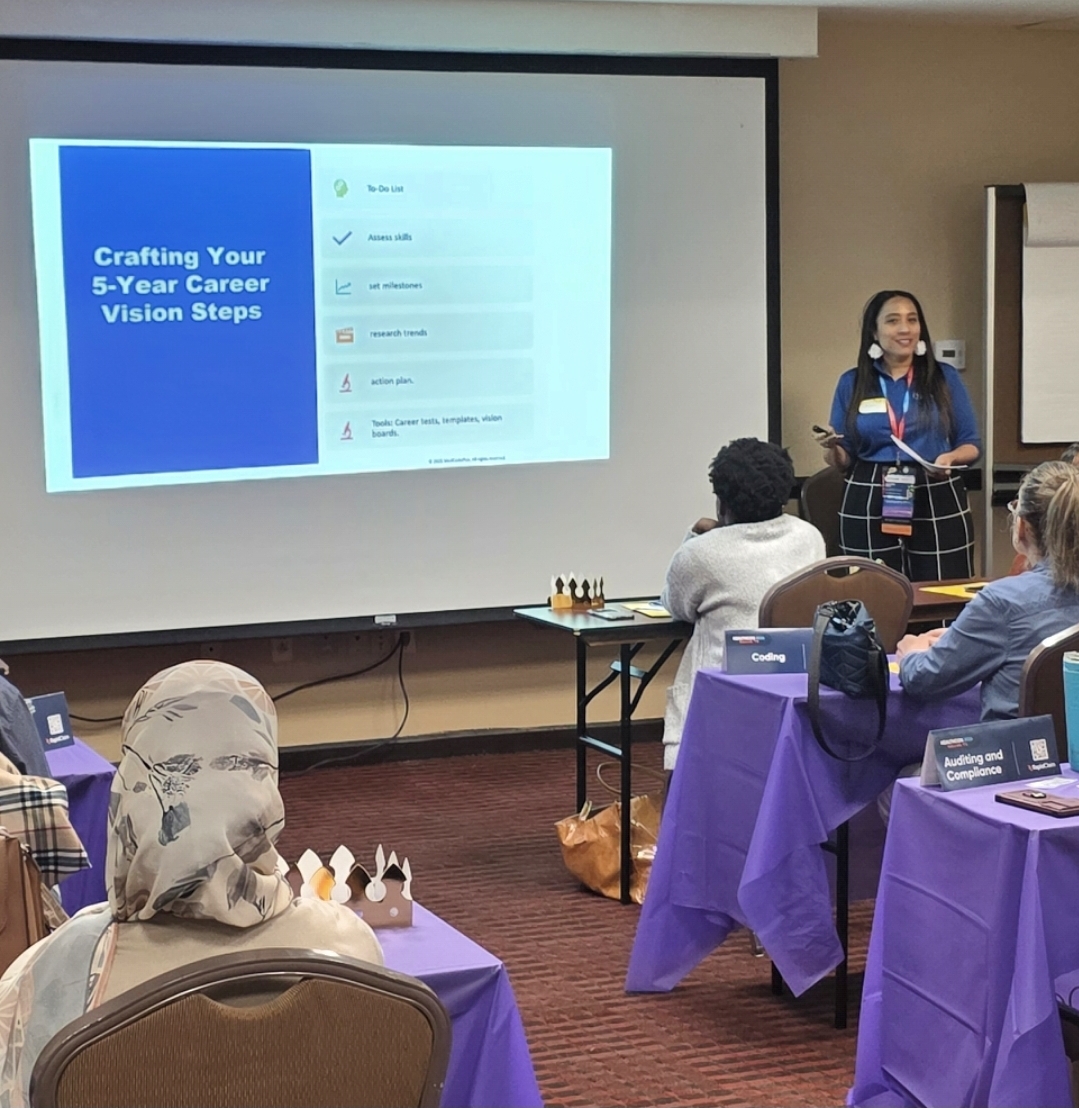 A woman presents a slide titled 'Crafting Your 5-Year Career Vision Steps' to an audience in a conference room with purple tablecloths.