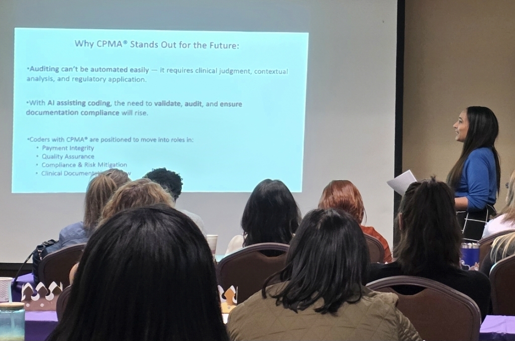 Woman presenting a PowerPoint slide to an audience in a conference room, with attendees seated and taking notes.