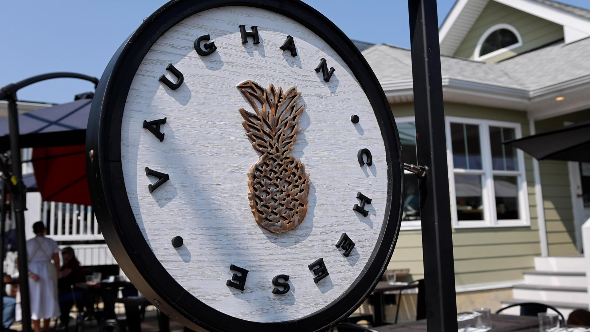 Round sign with pineapple logo and the words 'Vaughan Chise' around it, outside a house.