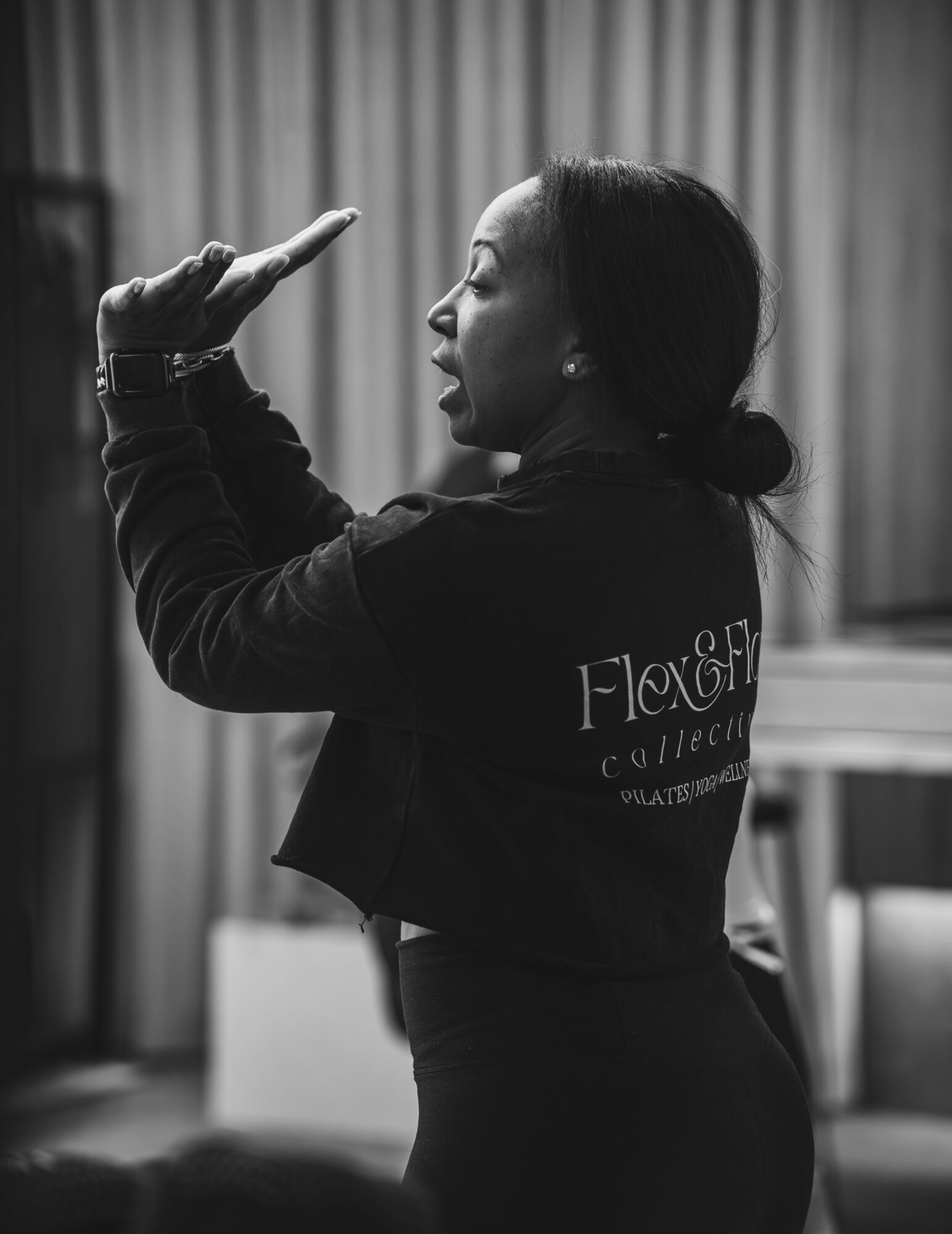 Side view of a woman with dark hair in a ponytail, gesturing with her hand, in a room with curtains and furniture