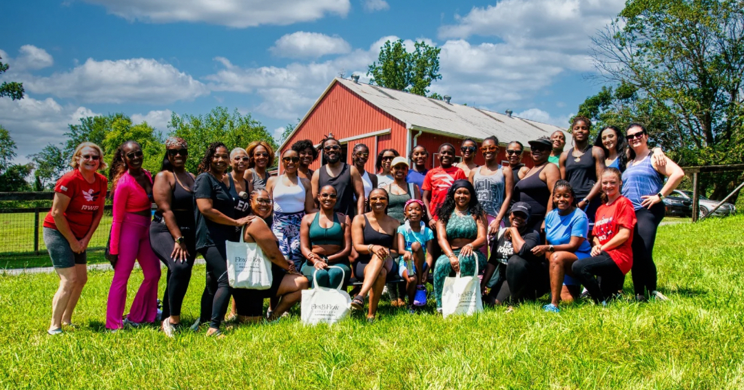 Group of people outdoors on grass in front of a red building, smiling and posing for a photo.