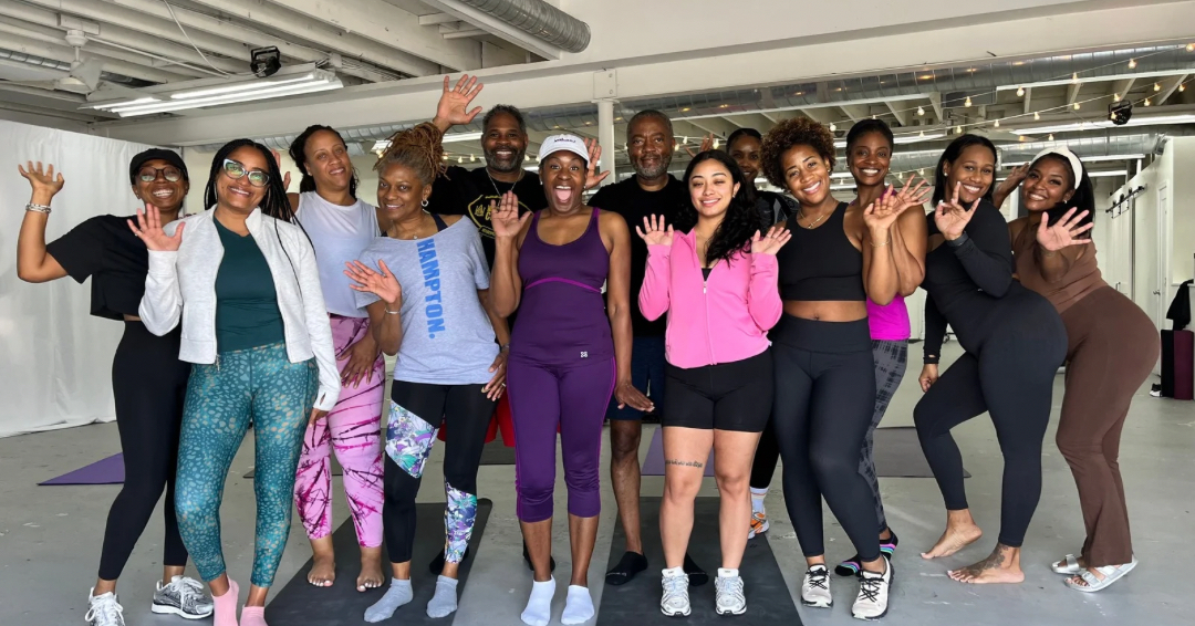 Group of ten women standing together in a fitness studio, smiling and posing for the photo.