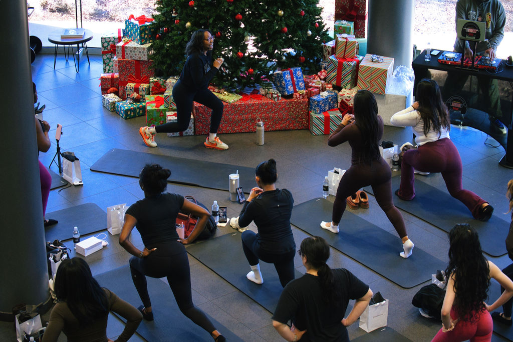 Group of people participating in a fitness class near a decorated Christmas tree with presents, in a spacious indoor setting.