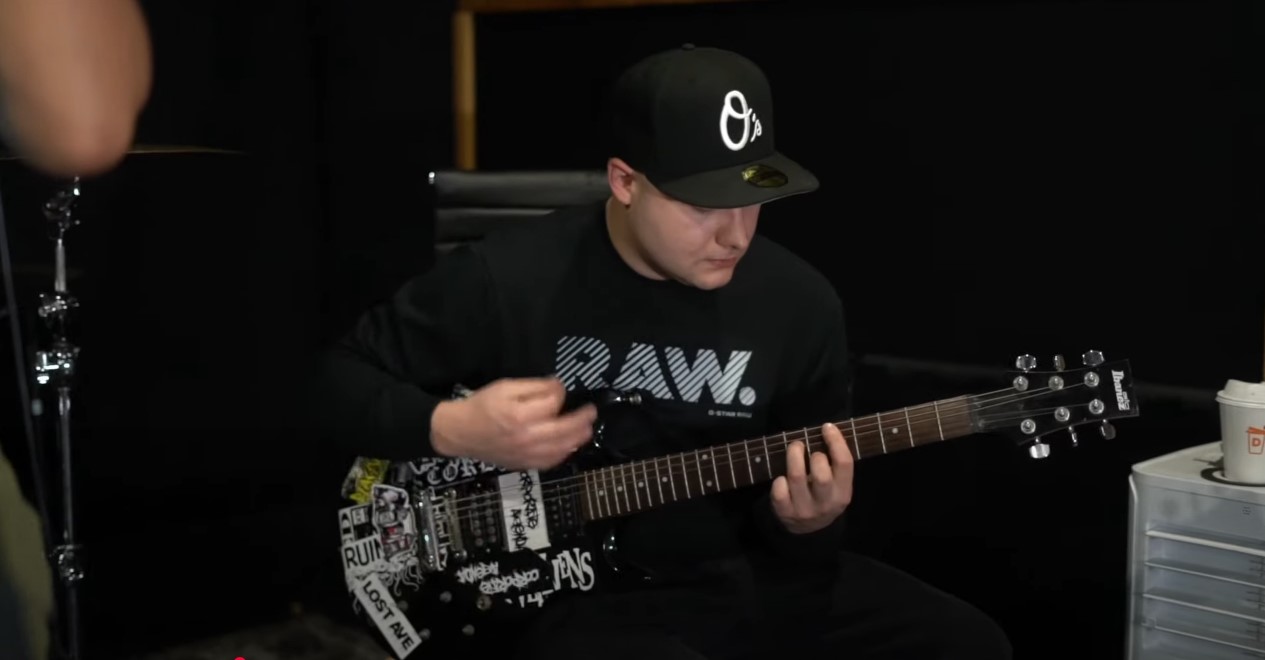 Person wearing a black cap and shirt playing an electric guitar in a recording studio.