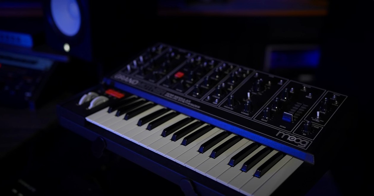 A synthesizer keyboard with control knobs and sliders, placed on a stand in a dark room.