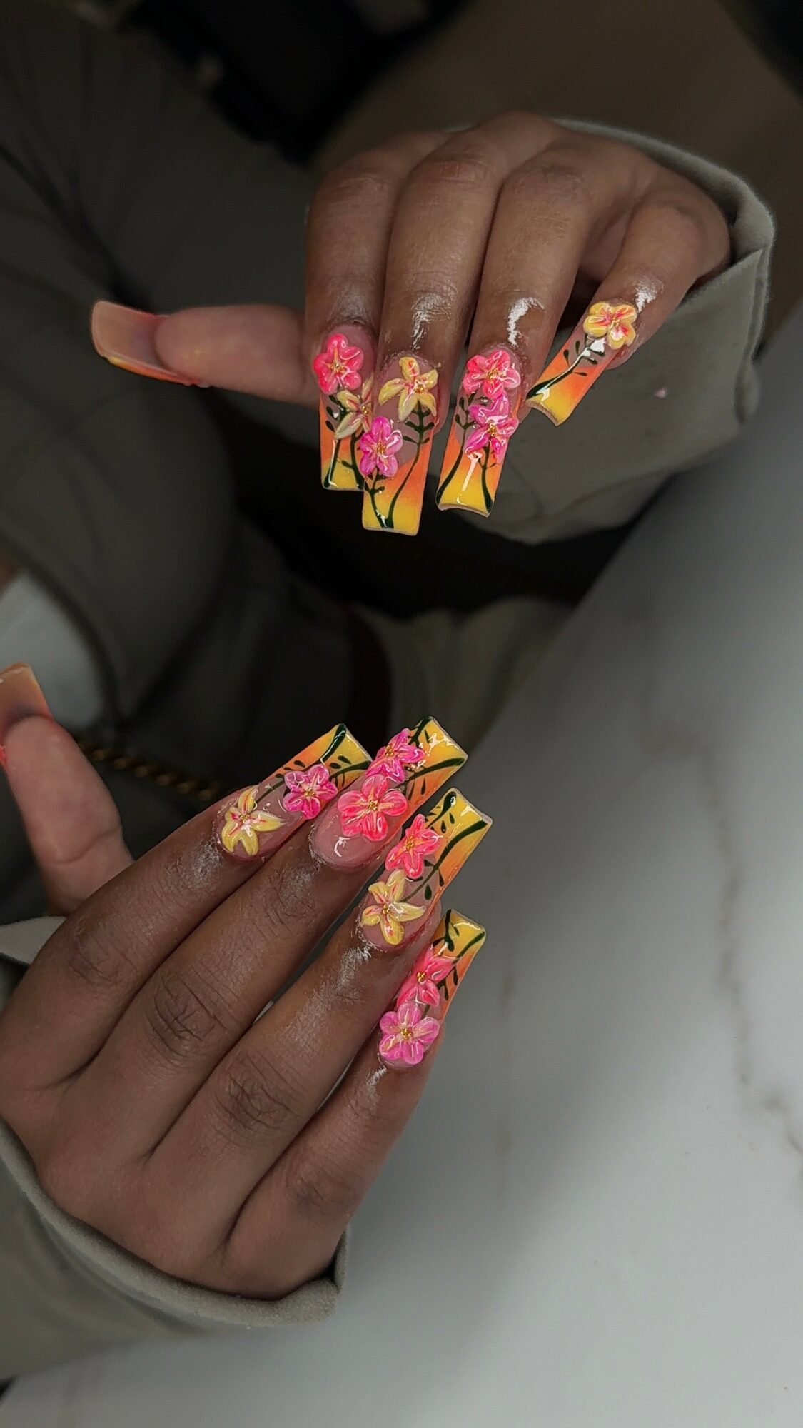 Close-up of hands with long, decorated nails featuring pink, orange, and yellow floral designs.