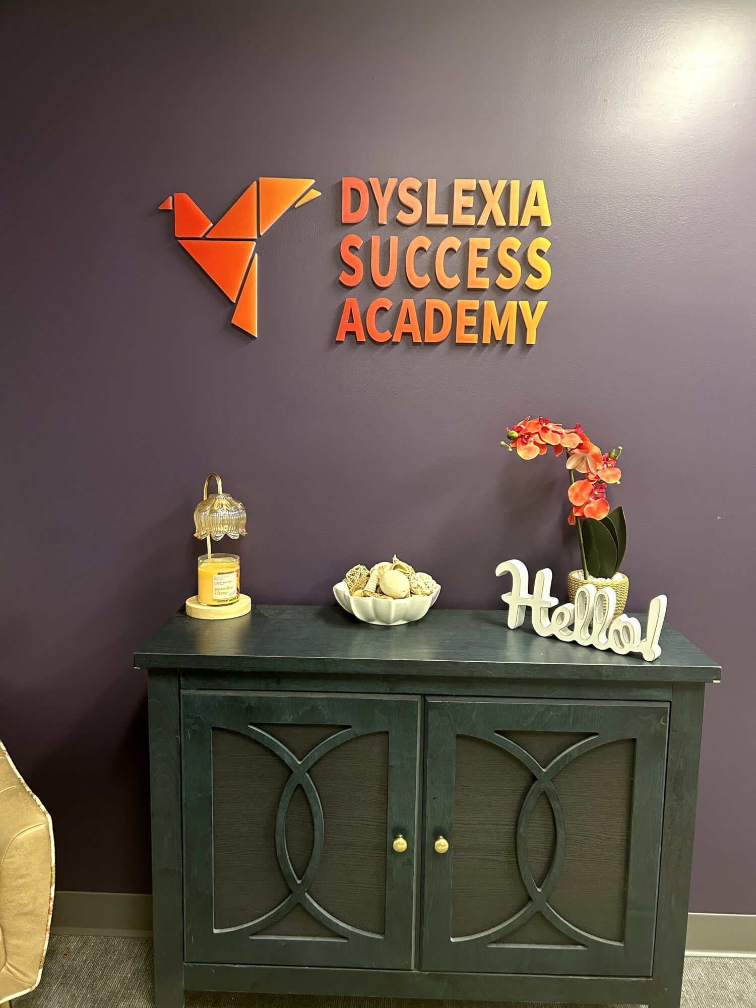 Wall with logo and text reading Dyslexia Success Academy, decorated with a candle, flowers, and a sign saying Hello.