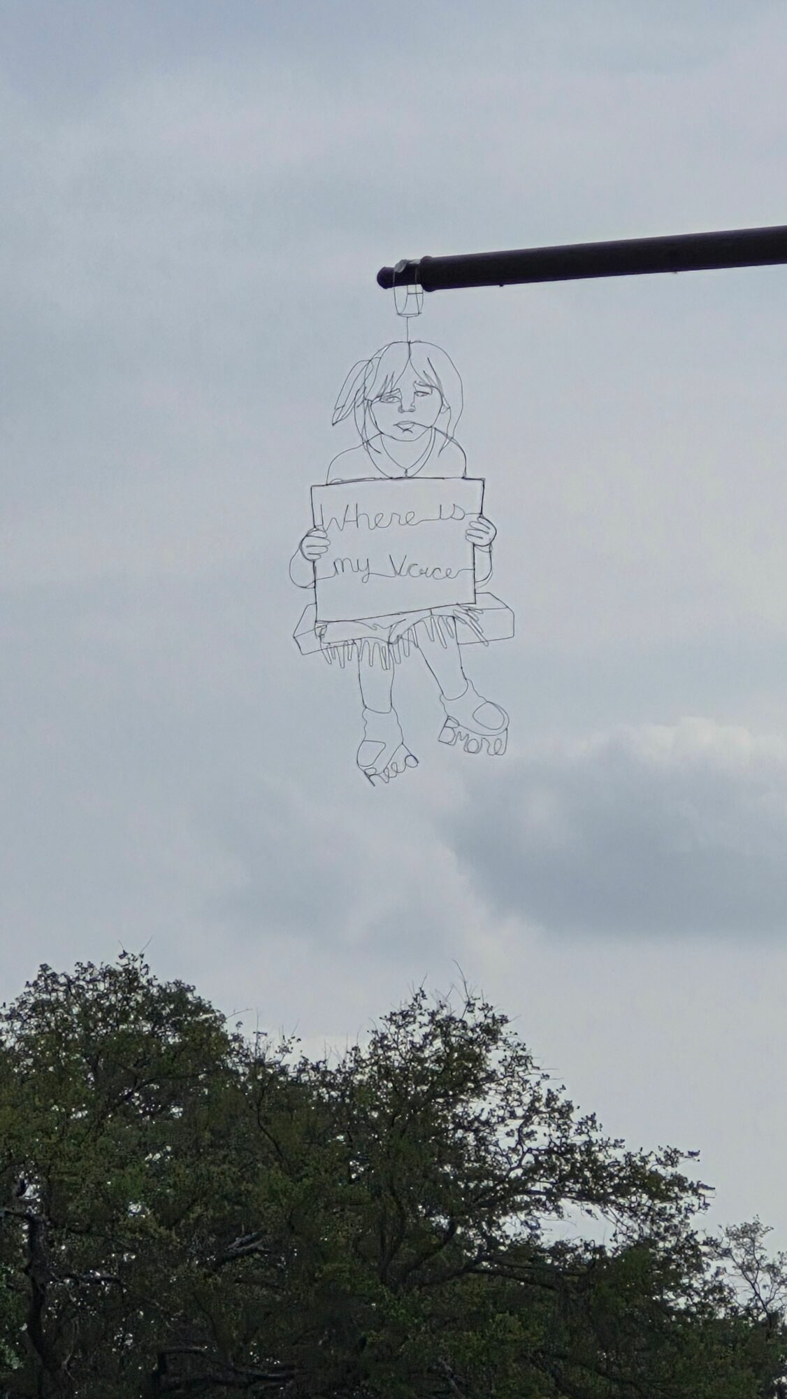 A wire outline of a person holding a sign, with trees and sky in the background.