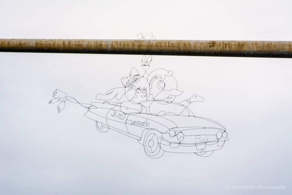 Pencil sketch of two characters in a car with a 'Just Married' sign, viewed from the side, with a horizontal rod above.