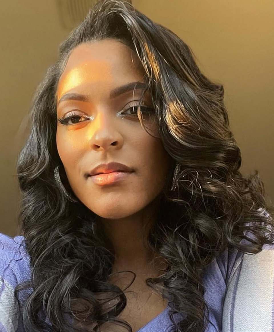 Portrait of a woman with wavy hair, looking at the camera, with warm lighting on her face.