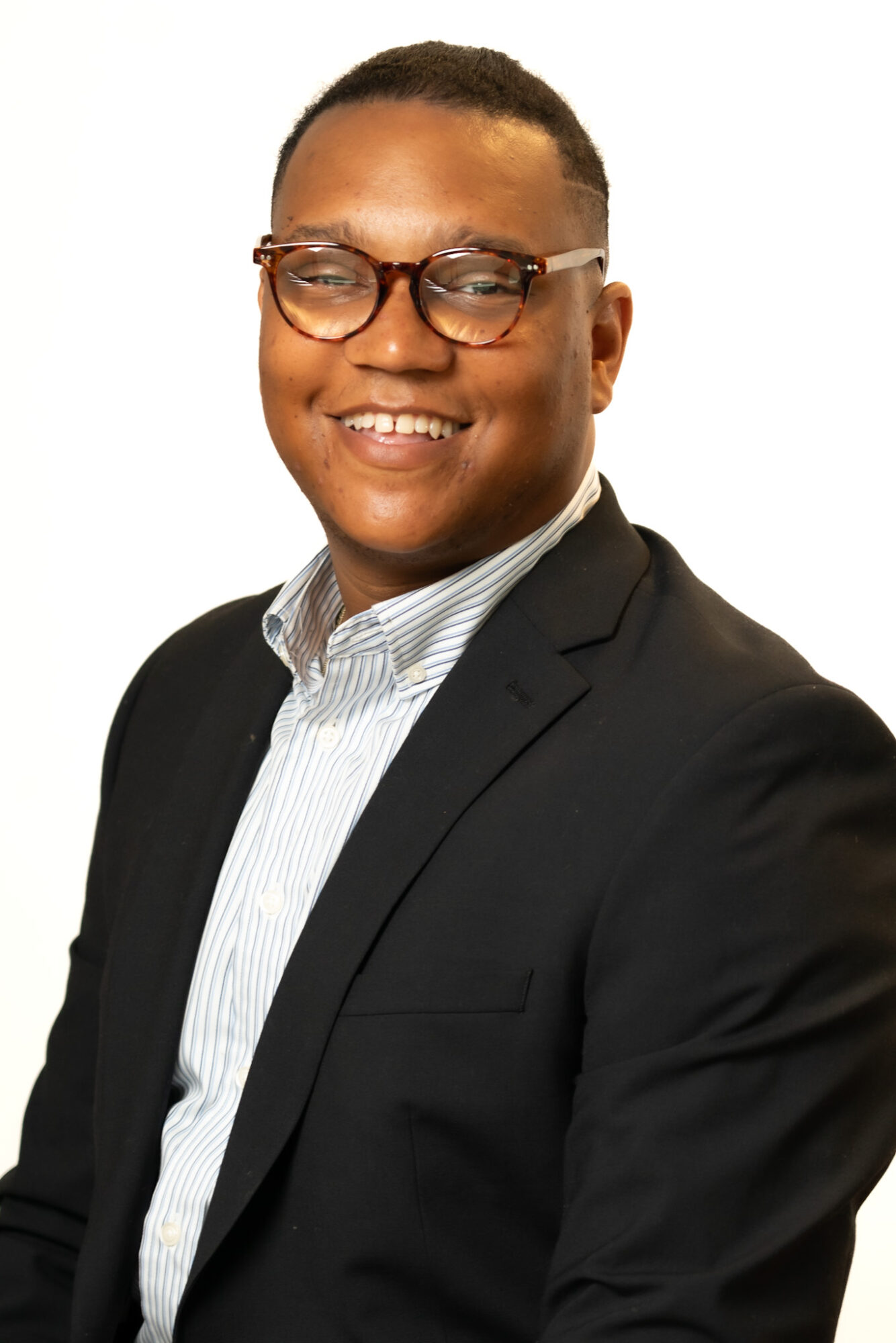 Person with glasses smiling, wearing a suit and striped shirt, facing forward against a white background.
