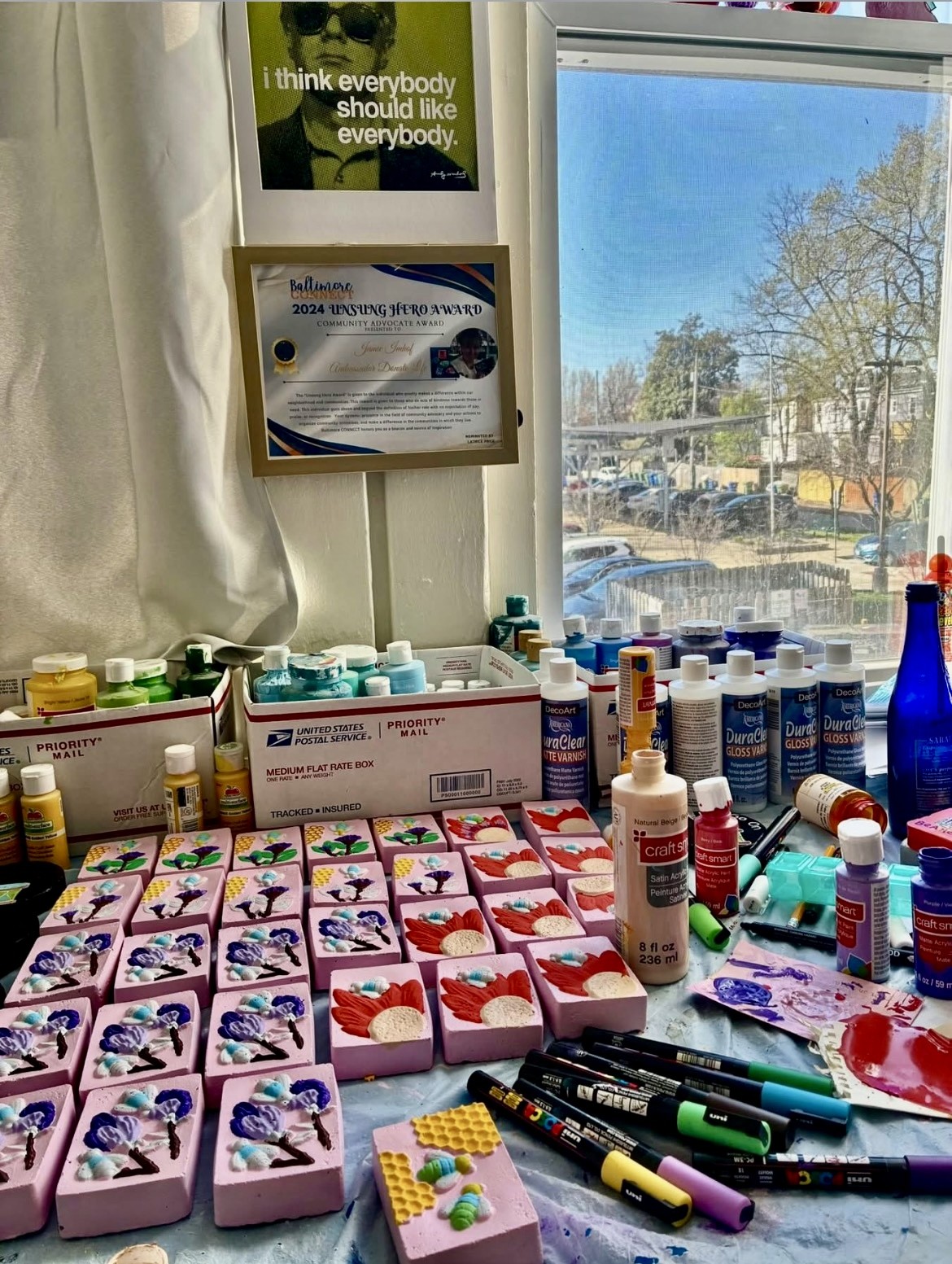 Display of colorful boxes, bottles, and markers on a table near a window with trees outside.