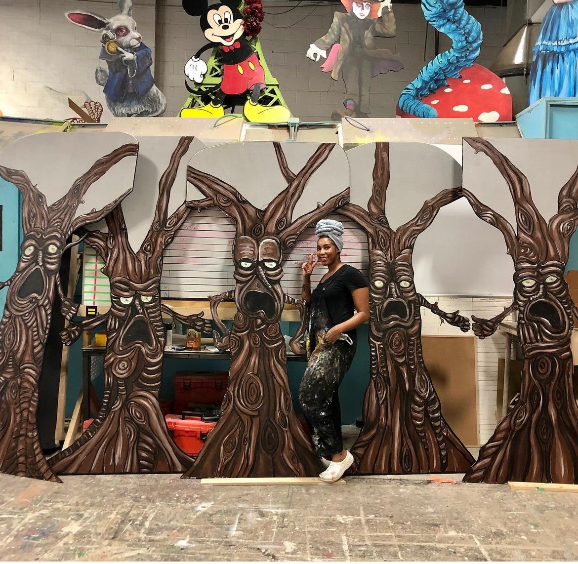 Person standing in front of a painted forest scene with large trees, cartoon characters above, and a wooden floor.